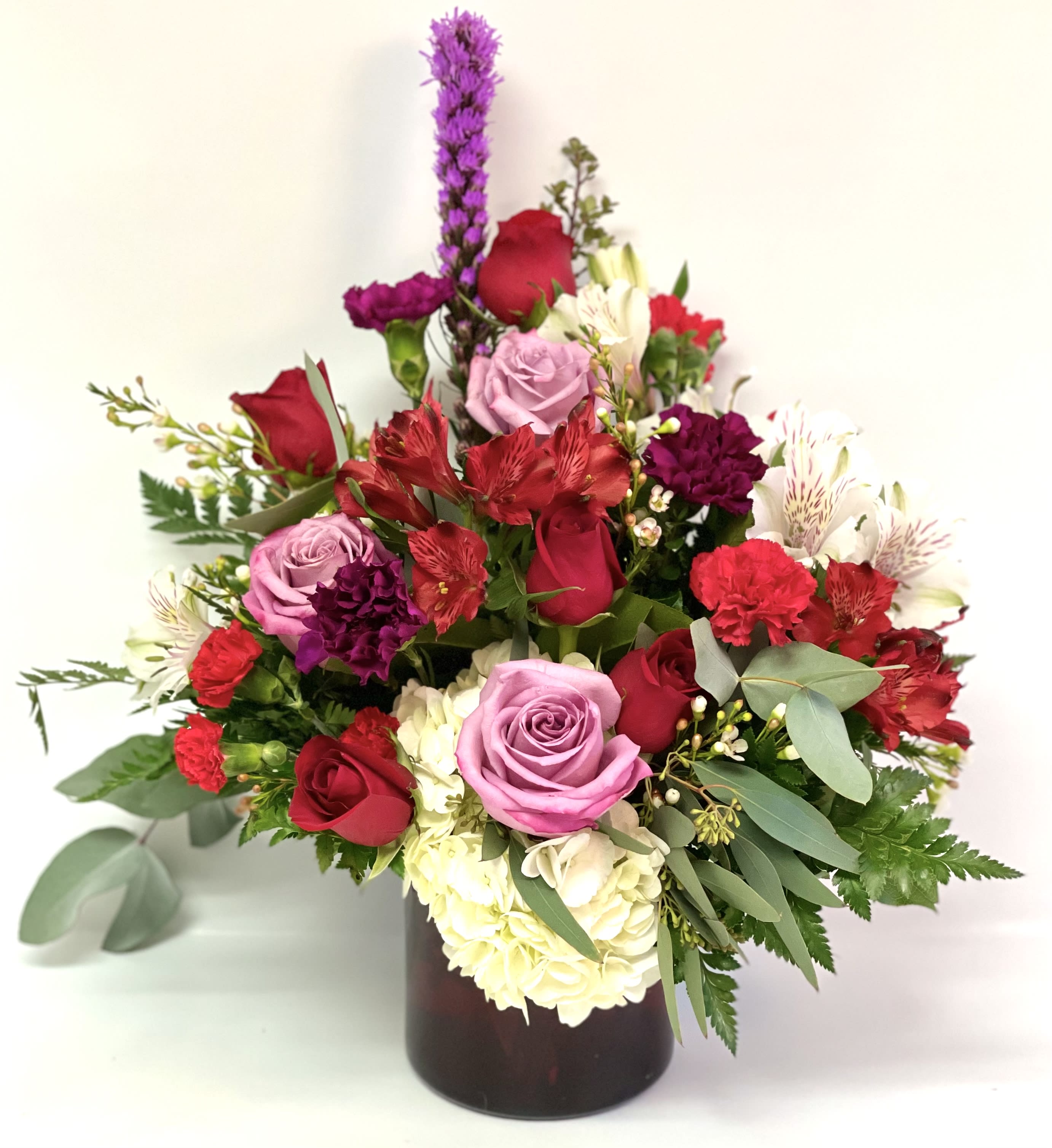 Mixed bouquet of roses, carnations, and alstroemeria in a dark vase