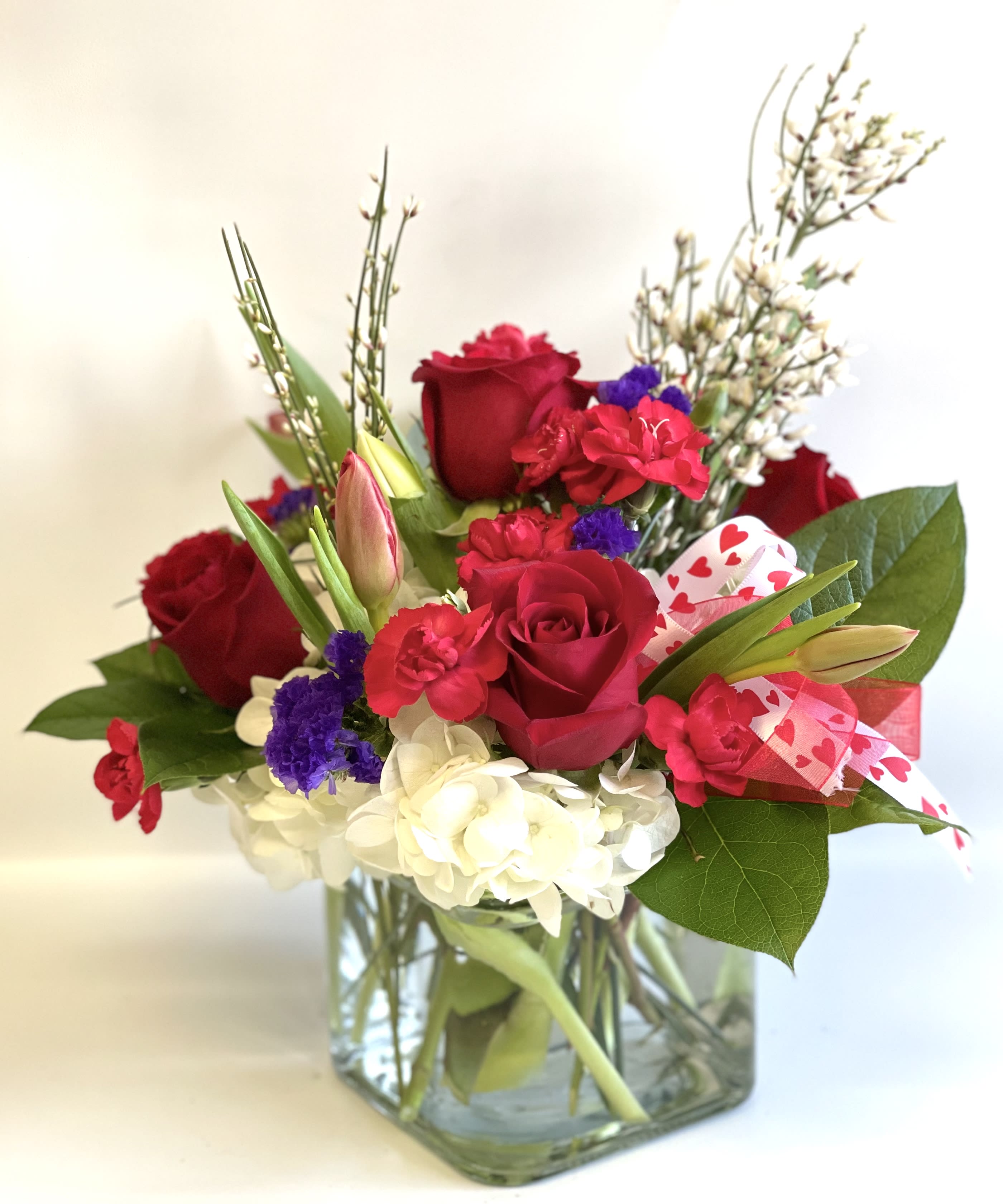 Red roses and mixed flowers in a square glass vase with heart ribbon