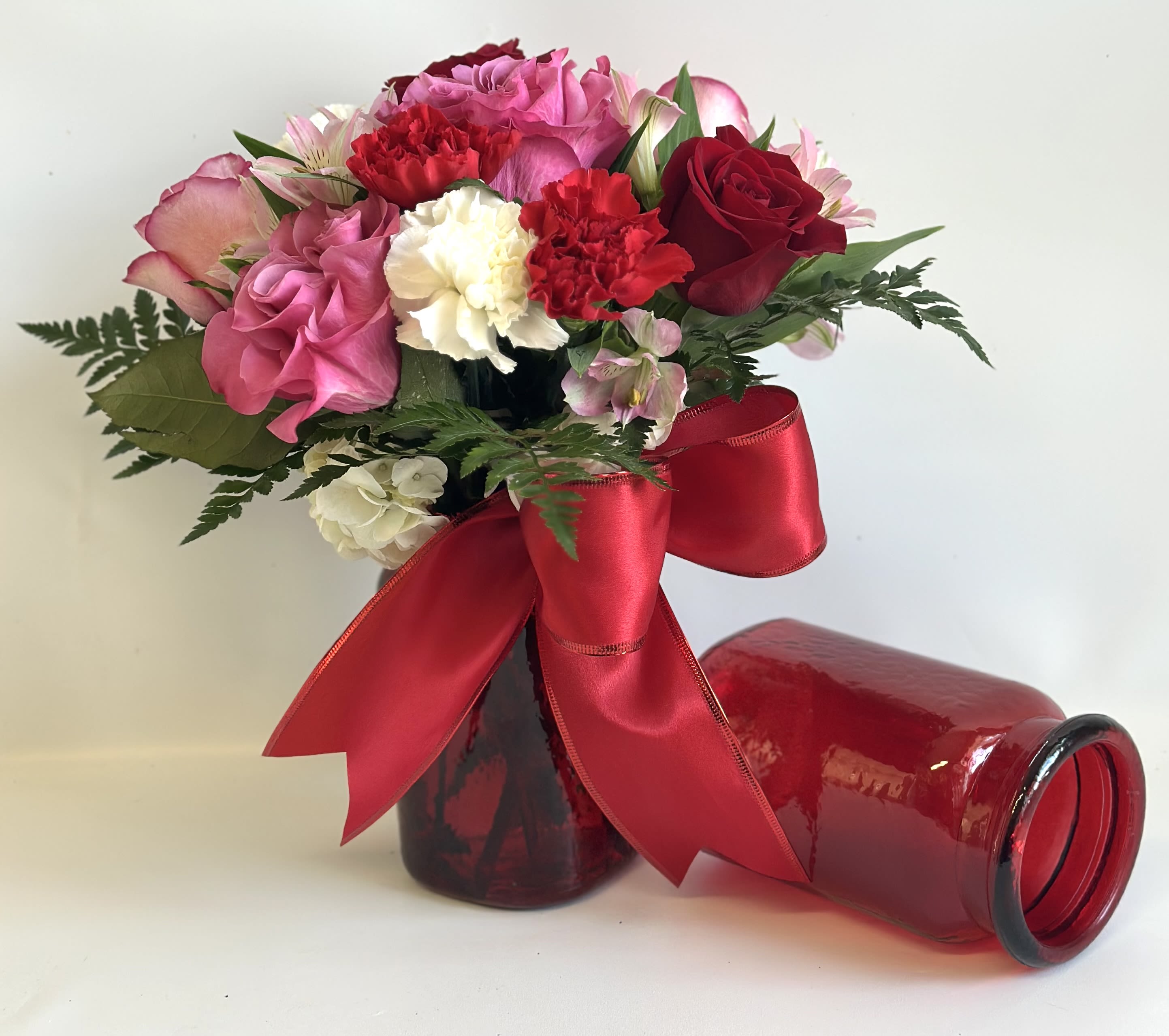 Pink and red bouquet in a red glass vase with a large ribbon