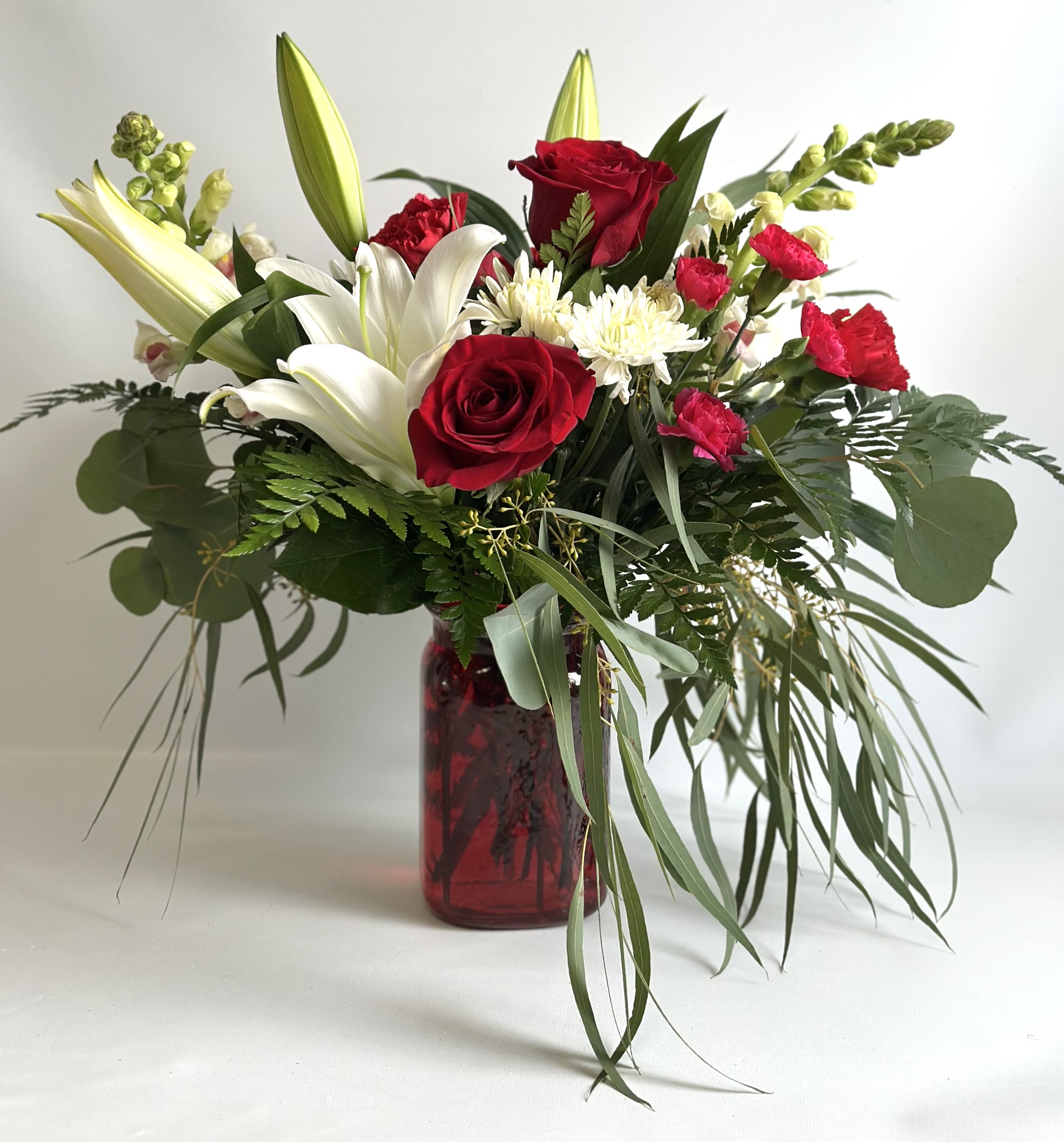 Bouquet of red roses, white lilies, and white mums in a red glass vase