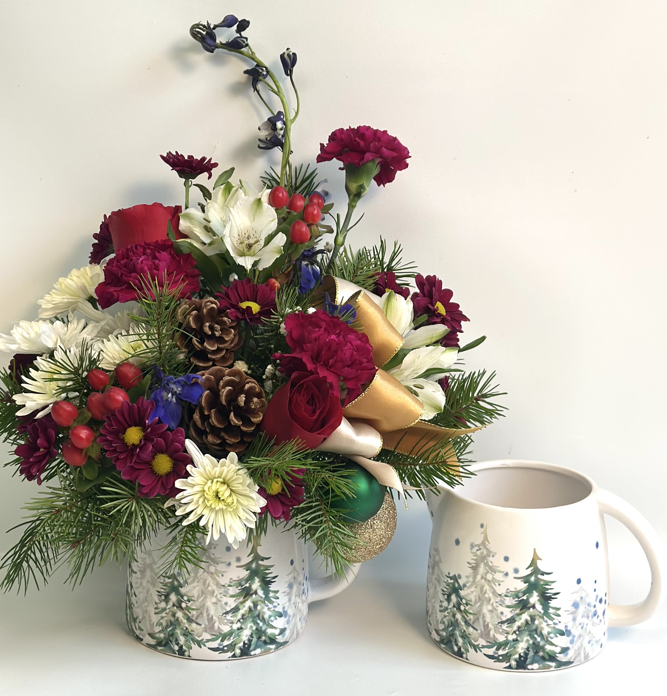 Holiday floral arrangement in a winter-themed mug beside a matching mug