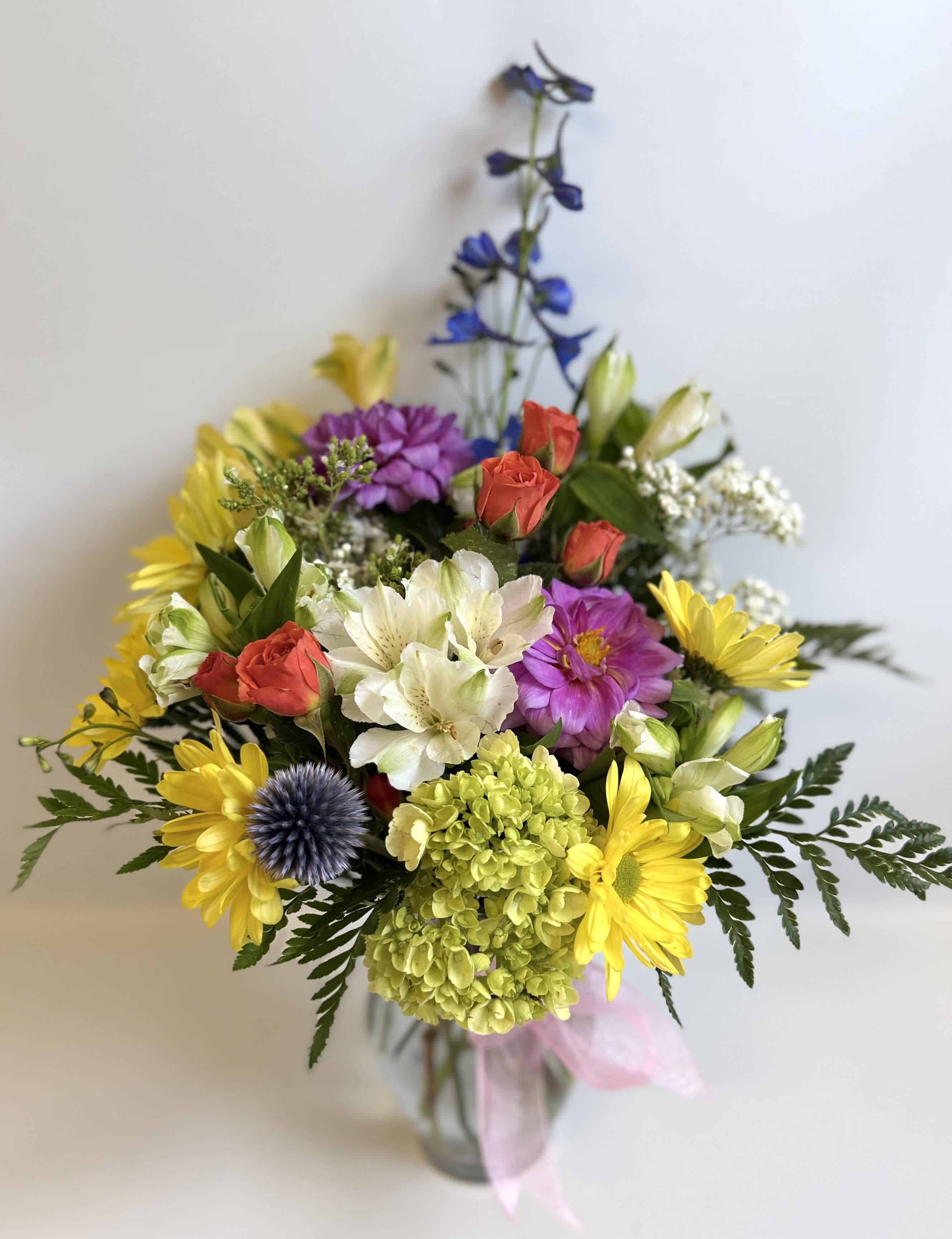 Mixed bouquet of yellow daisies, roses, and purple flowers in a glass vase