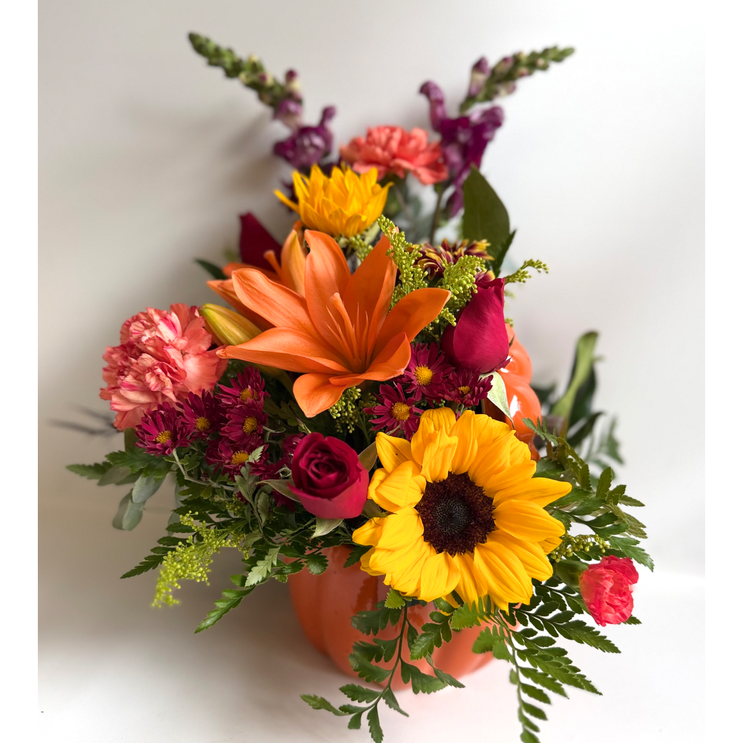 Colorful mixed bouquet in an orange vase with sunflowers, lilies, roses, and carnations