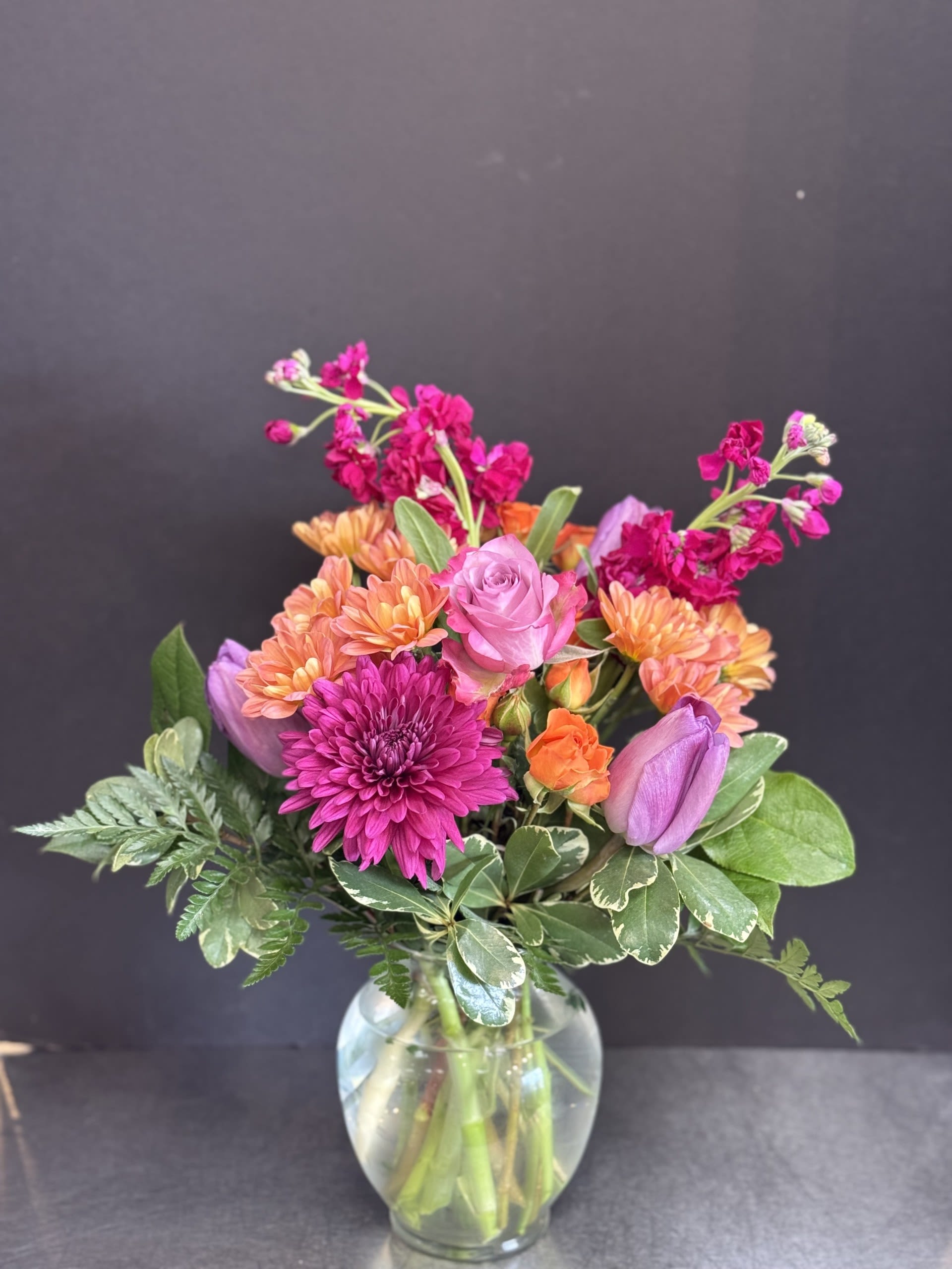 Mixed bouquet of pink, orange, and purple flowers in a glass vase