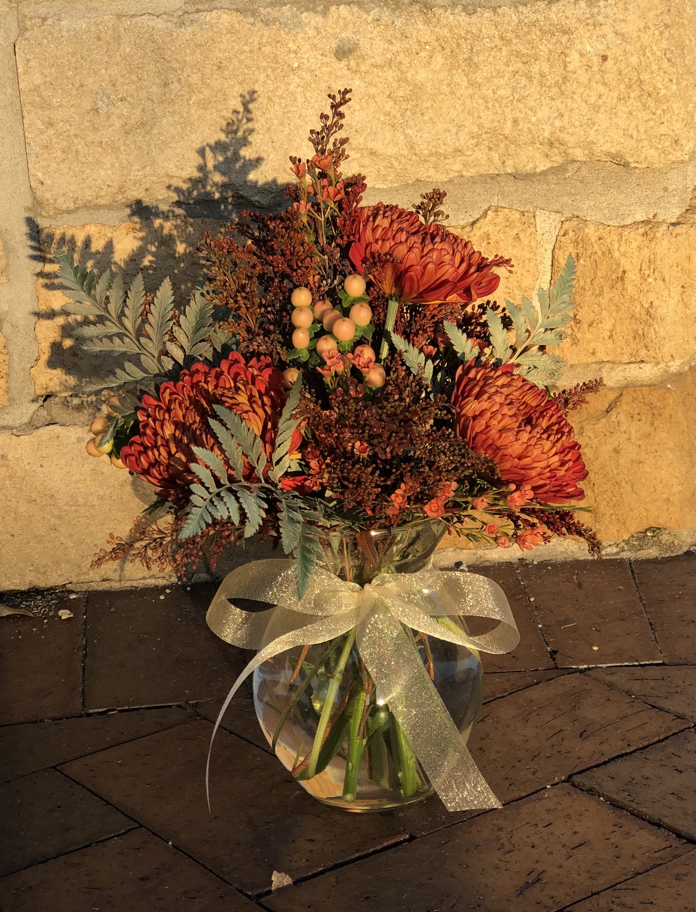 Orange chrysanthemum bouquet in a glass vase with a gold ribbon