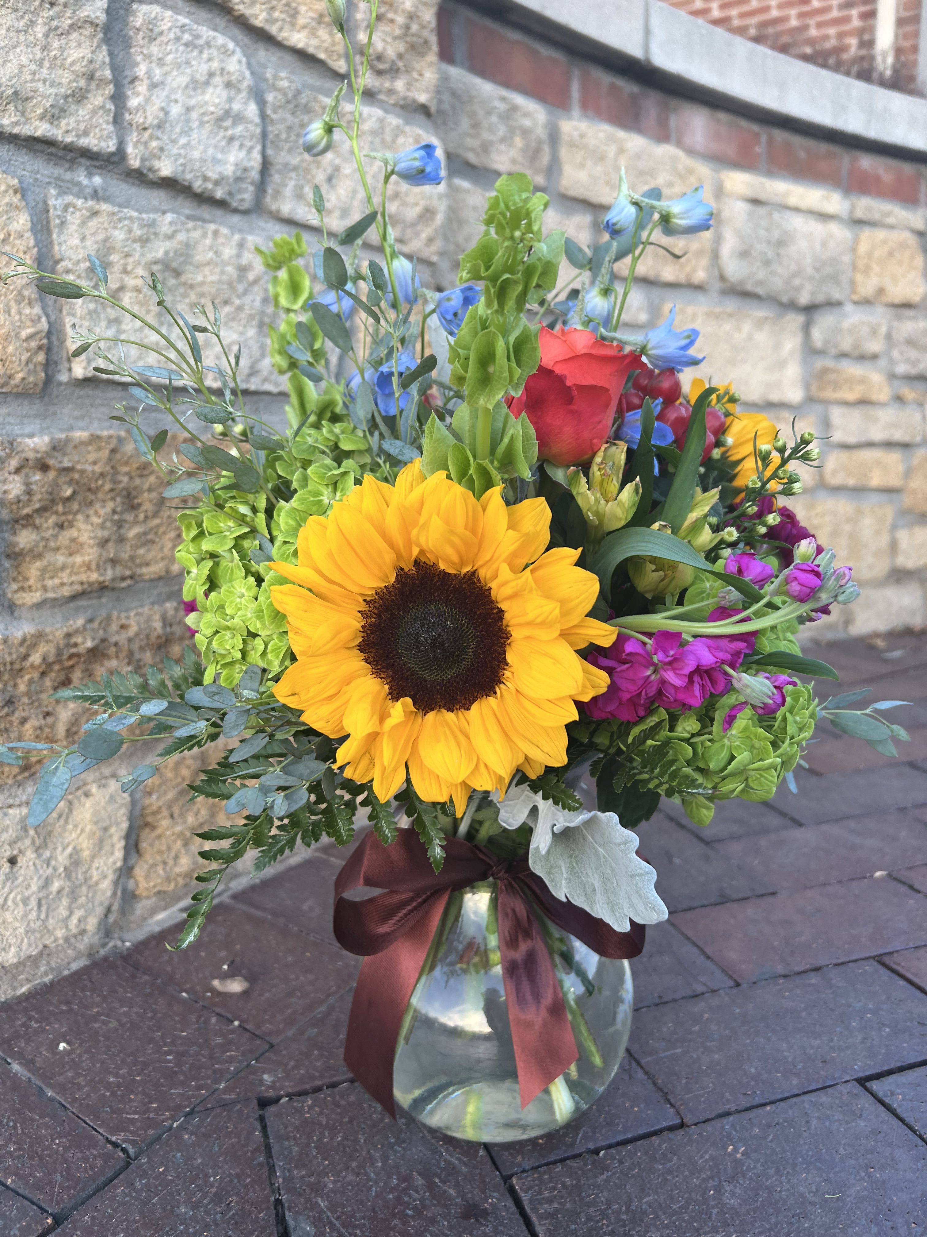 Mixed bouquet with a sunflower in a glass vase tied with a burgundy ribbon