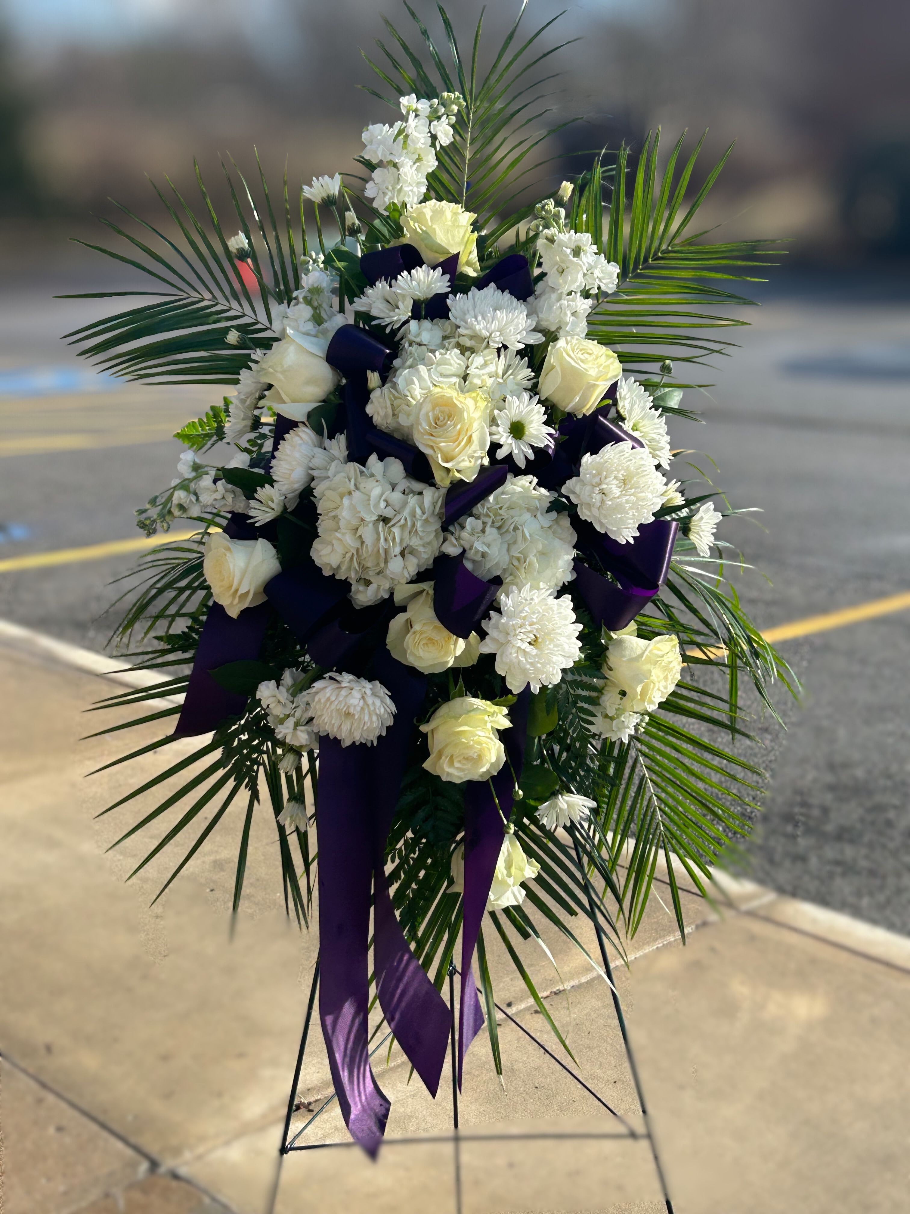 White floral standing spray with purple ribbon accents and palm fronds