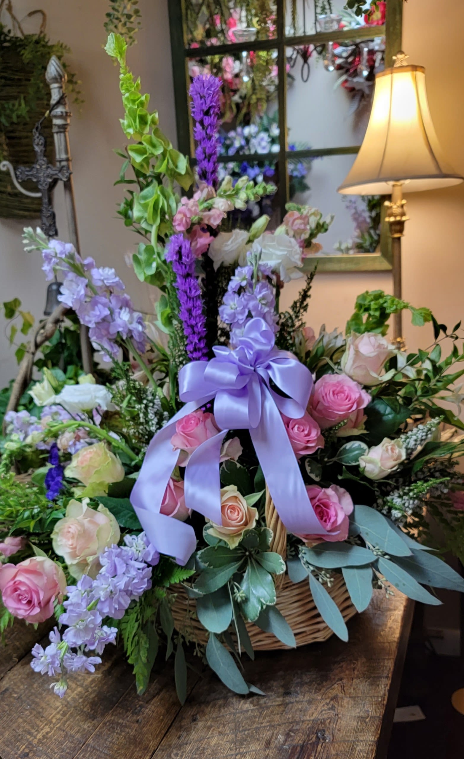 Basket arrangement of pink and lavender roses with a purple ribbon