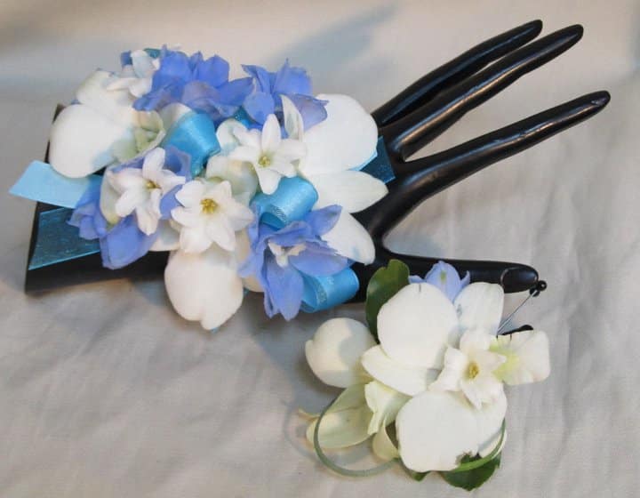 Two small floral corsages with blue and white flowers on black display hands.
