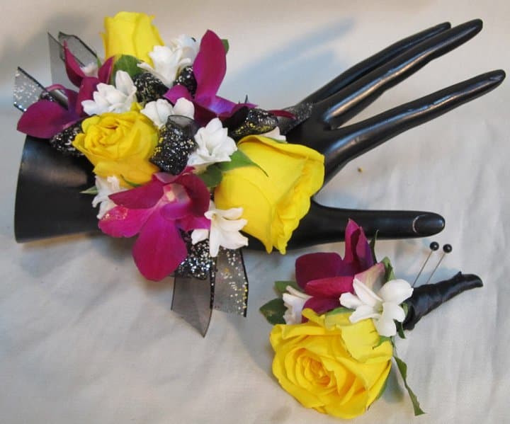 Yellow and magenta floral corsage and boutonniere on black display hands