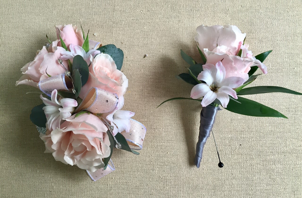 Two pale pink floral boutonnieres with ribbon and greenery on a beige background