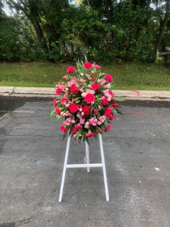 Standing floral wreath of pink and red flowers on a white easel