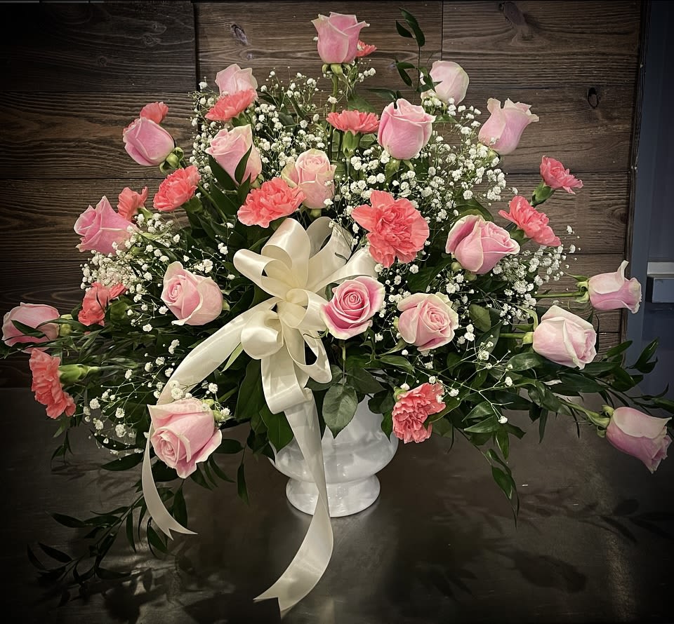 Pink roses and carnations in a white vase with a cream ribbon