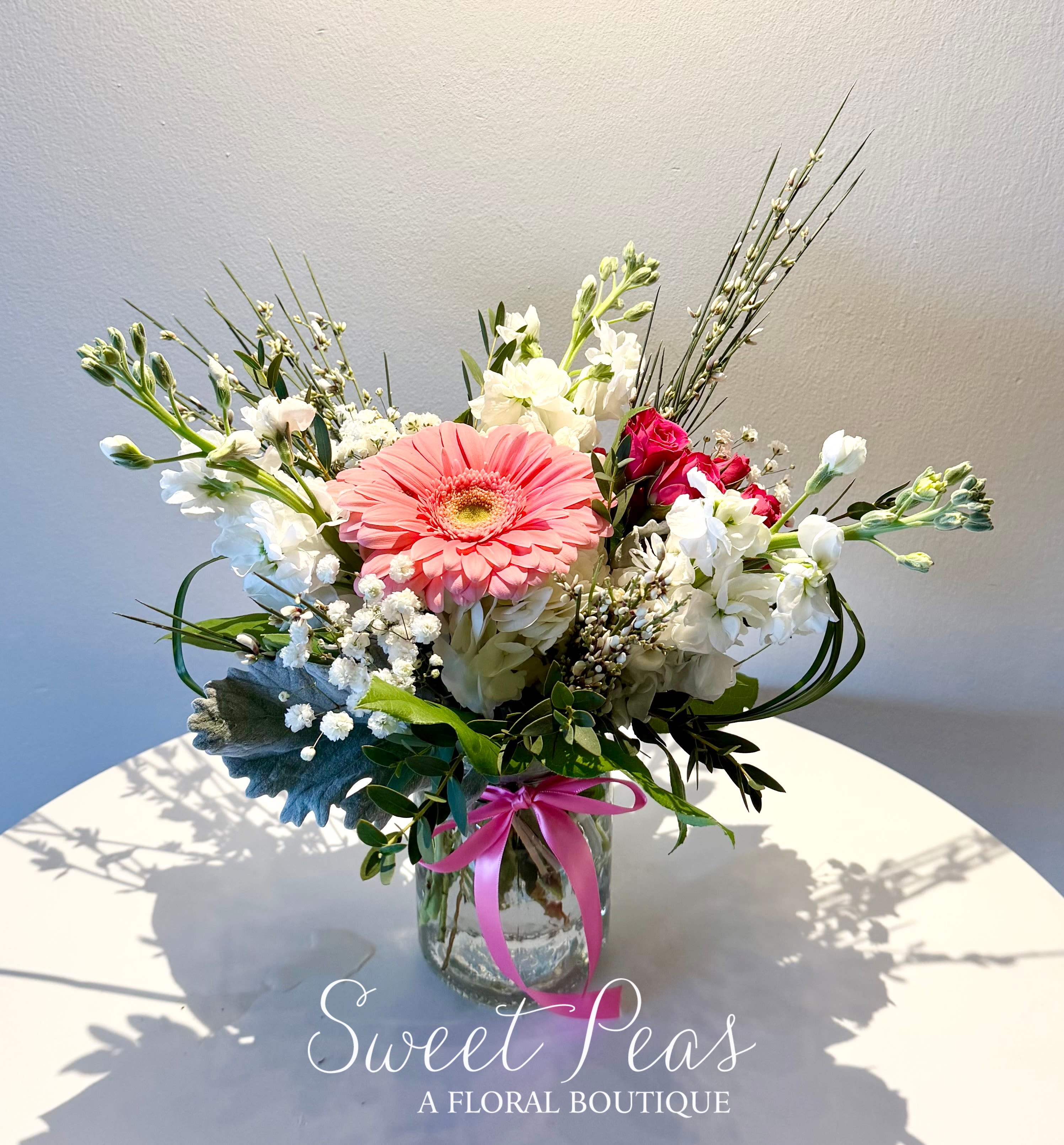 Pink gerbera bouquet in a glass vase with white blooms and a ribbon