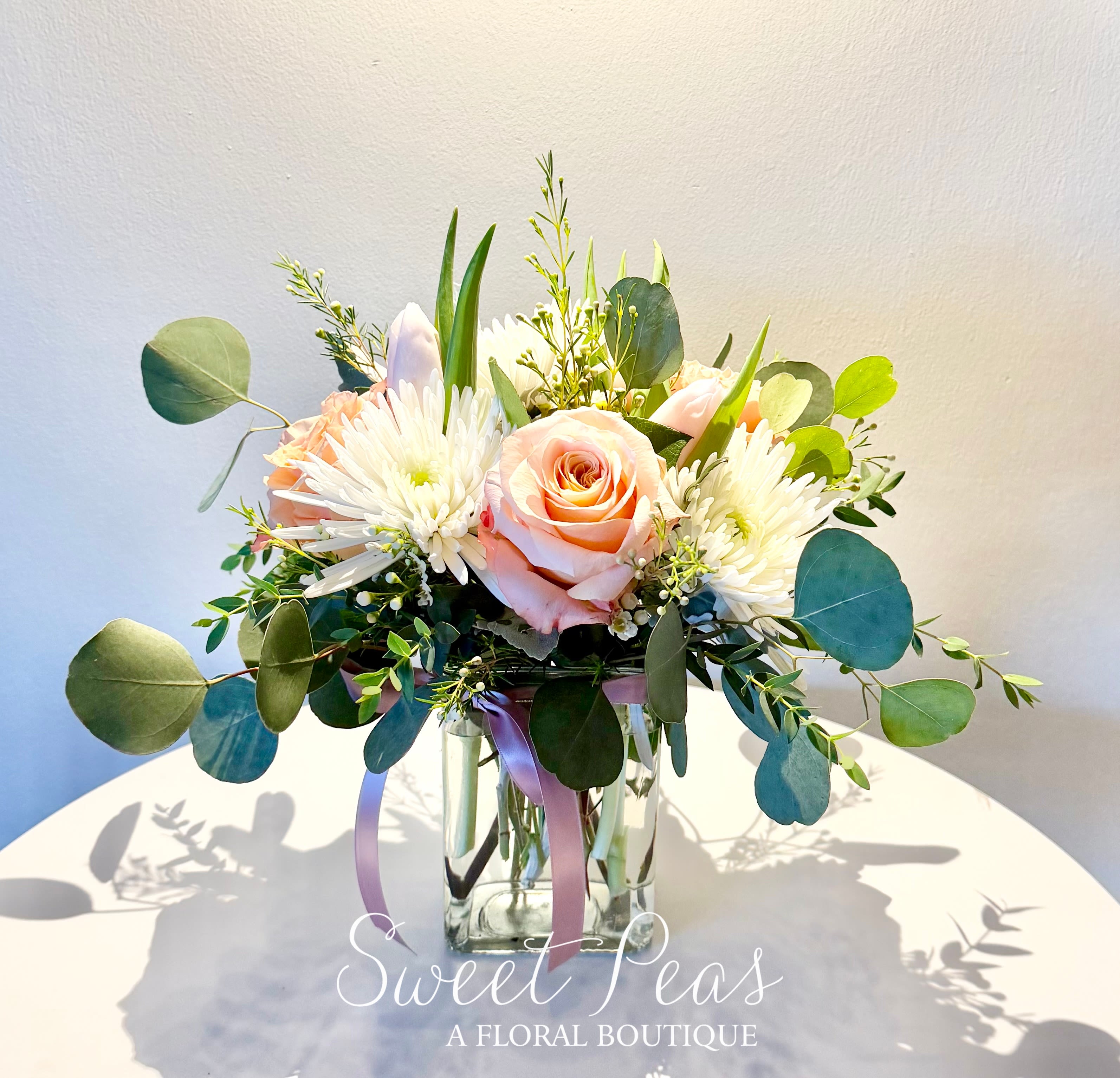 Peach roses and white flowers in a clear glass vase with eucalyptus