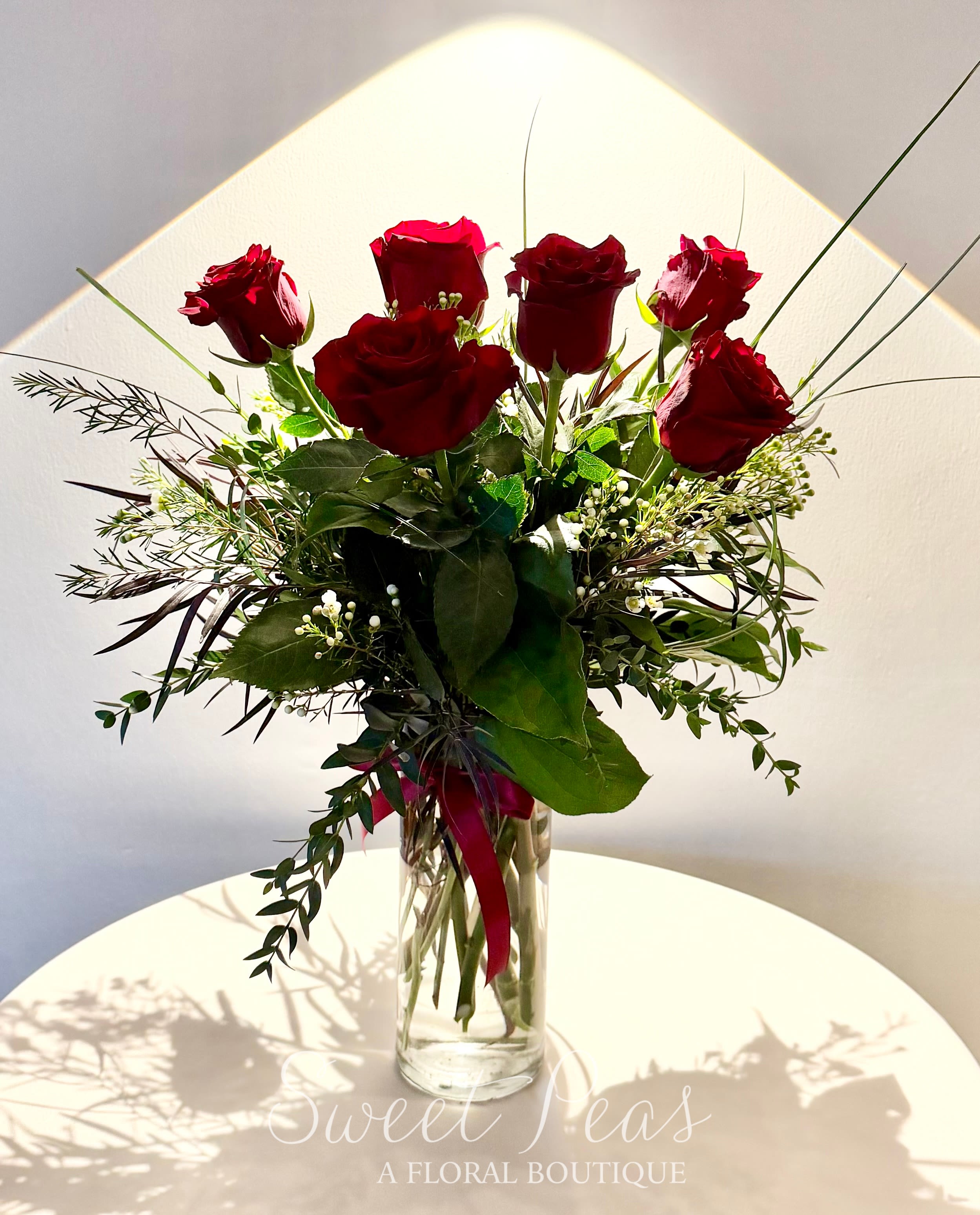 Red roses arranged in a clear glass vase with greenery