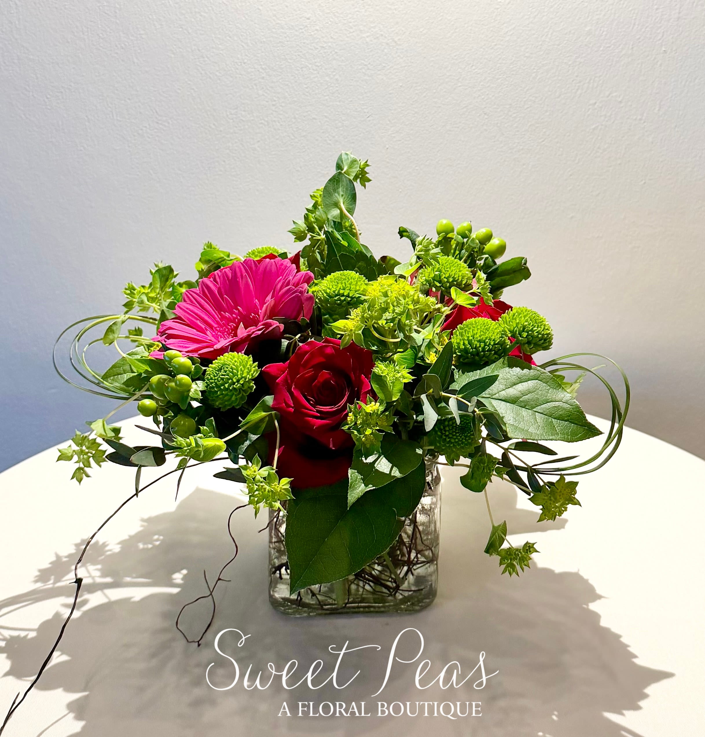 Mixed floral arrangement with red roses and a pink gerbera daisy in a glass vase
