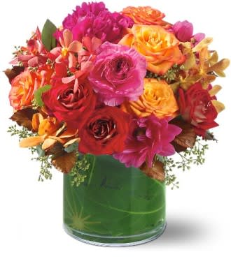 Bright mixed bouquet of roses and orchids in a green glass vase