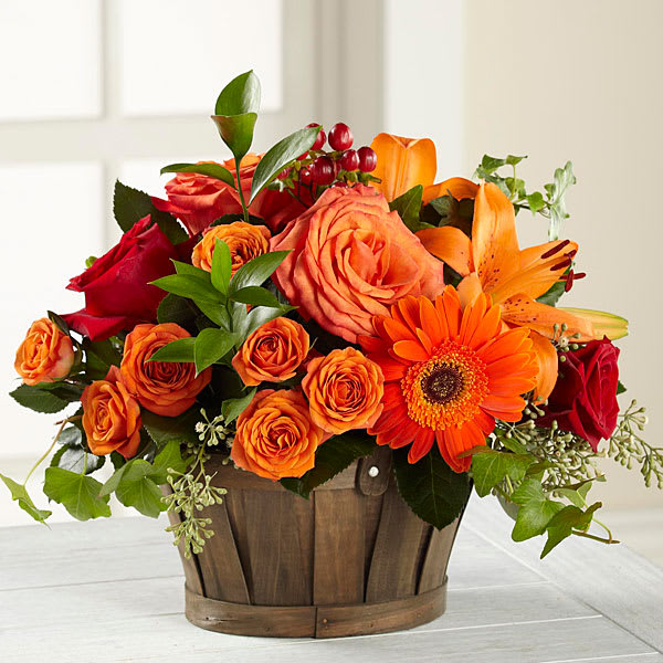Orange and red roses with a gerbera daisy in a wooden basket