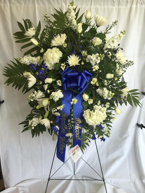Large white floral standing wreath with blue ribbon on an easel