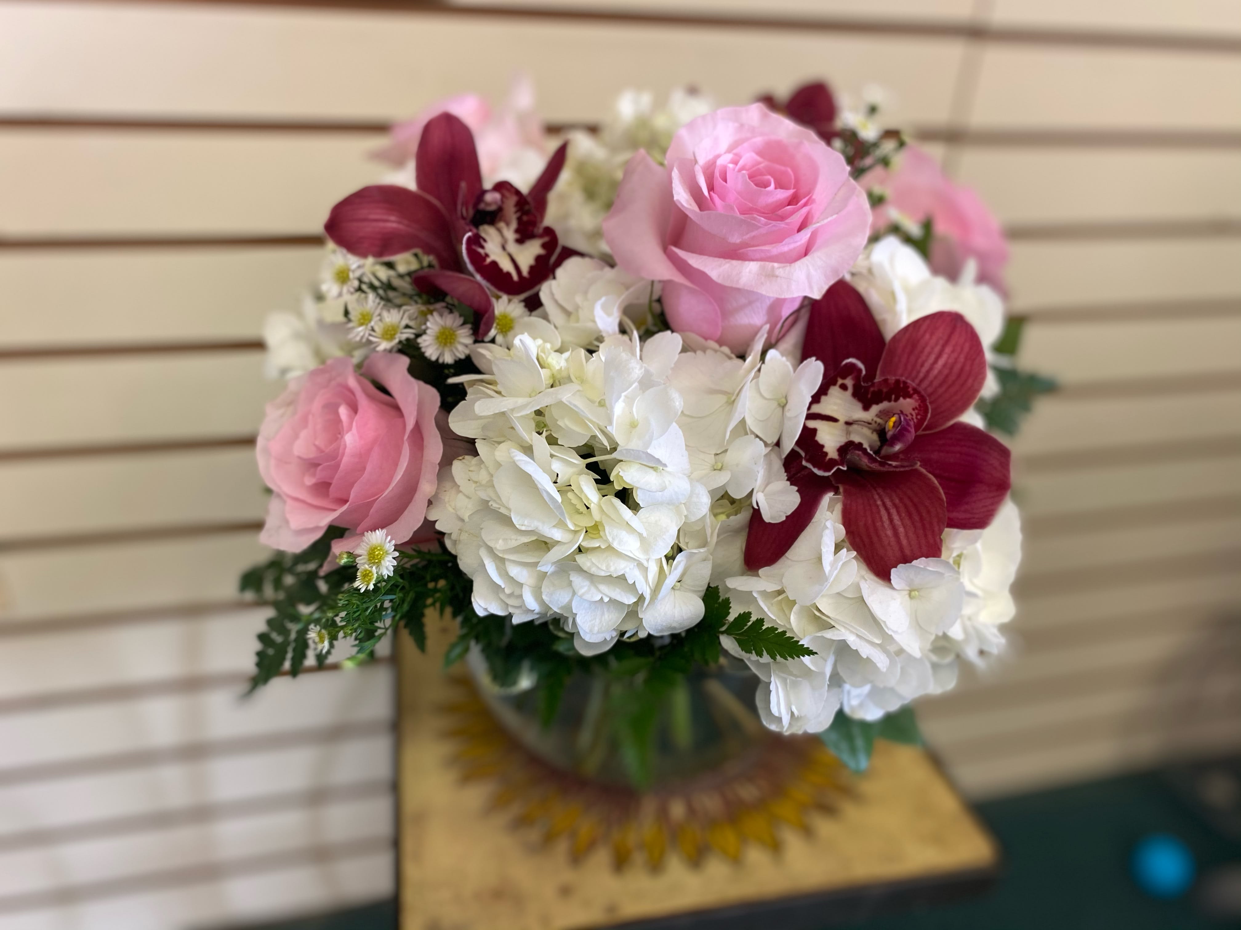 Pink roses and white hydrangeas with burgundy orchids in a glass vase
