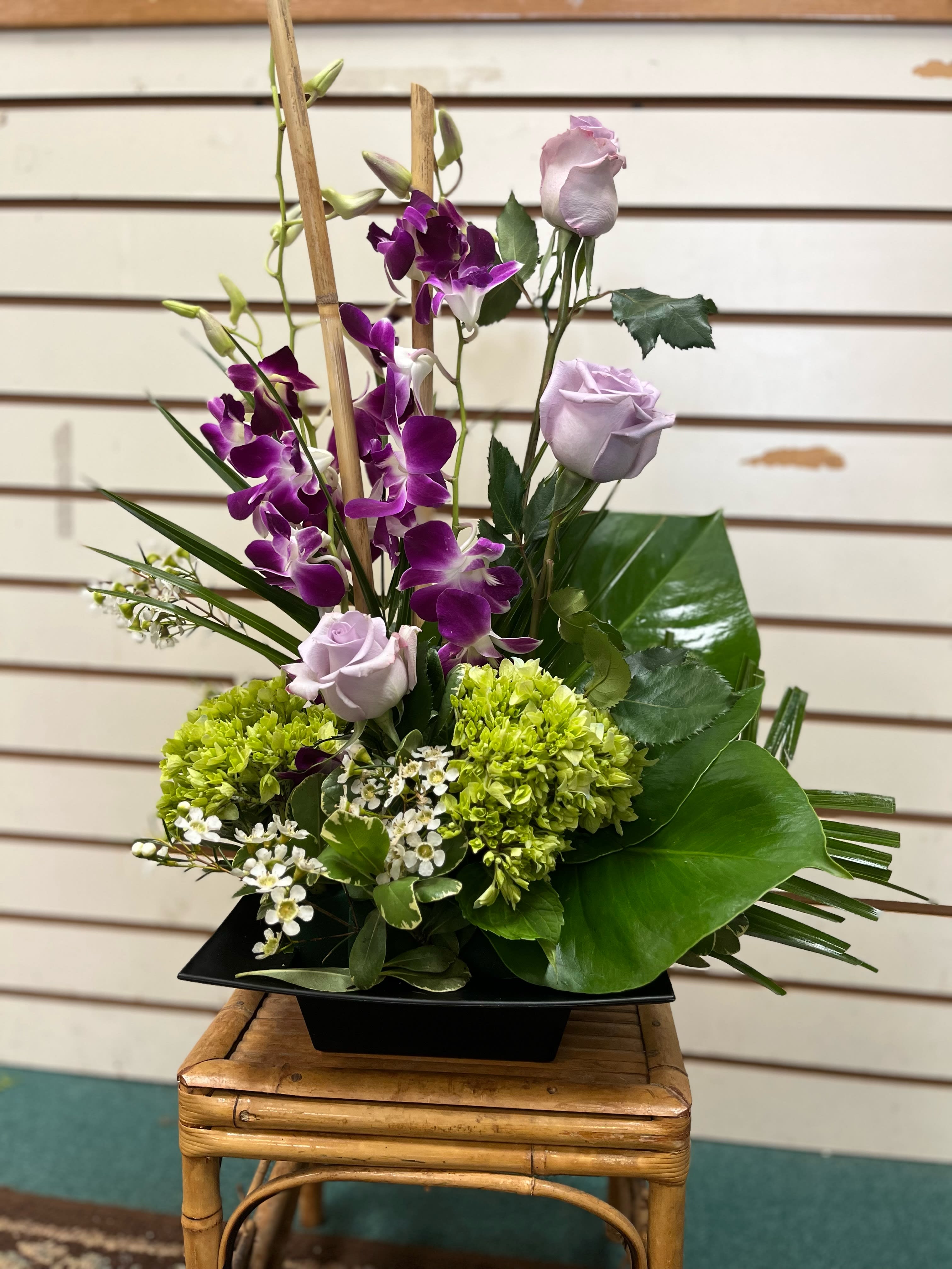 Purple orchids and pale lavender roses in a black vase