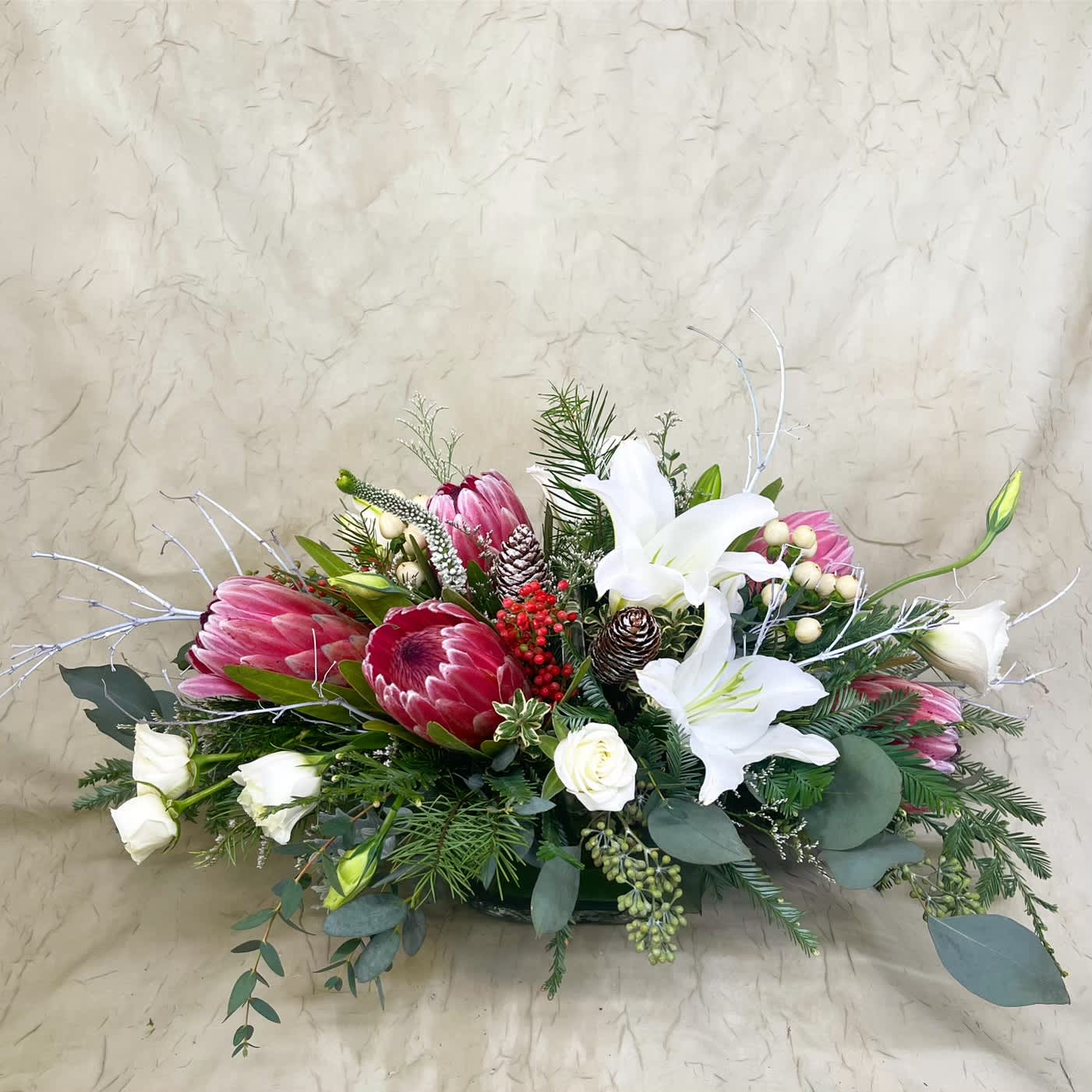Low floral arrangement with pink protea and white lilies in a shallow container