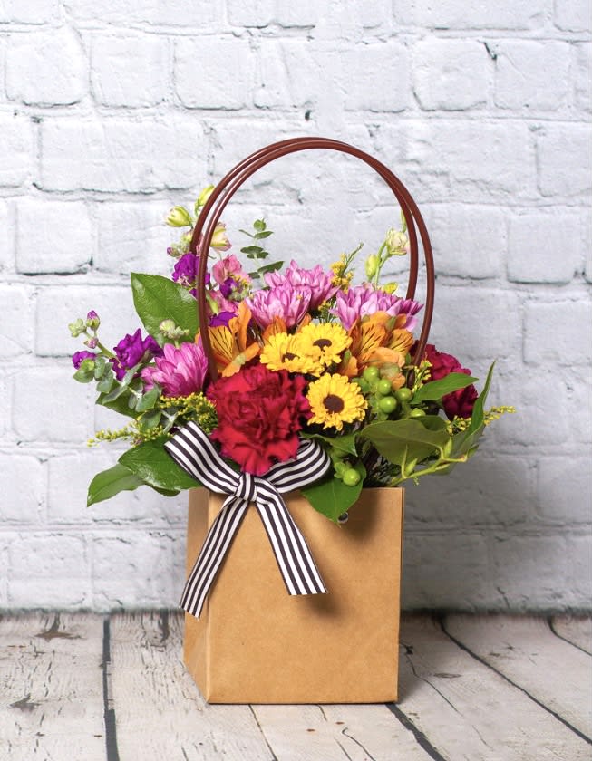 Mixed flower arrangement in a brown gift bag with a striped ribbon