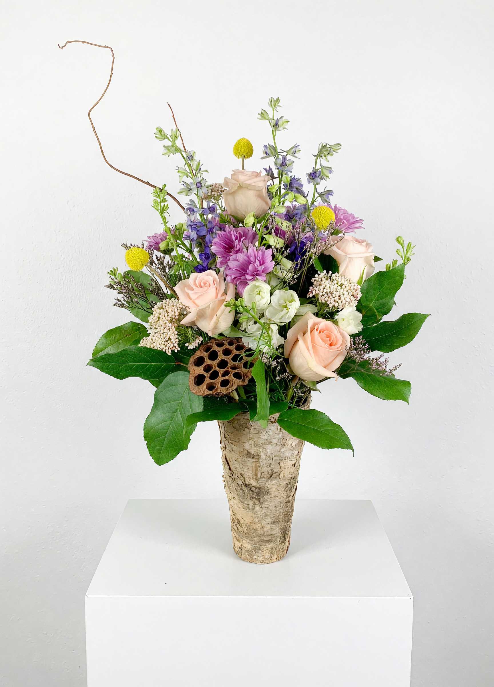 Mixed bouquet of roses, purple blooms, and yellow accents in a birch-style vase