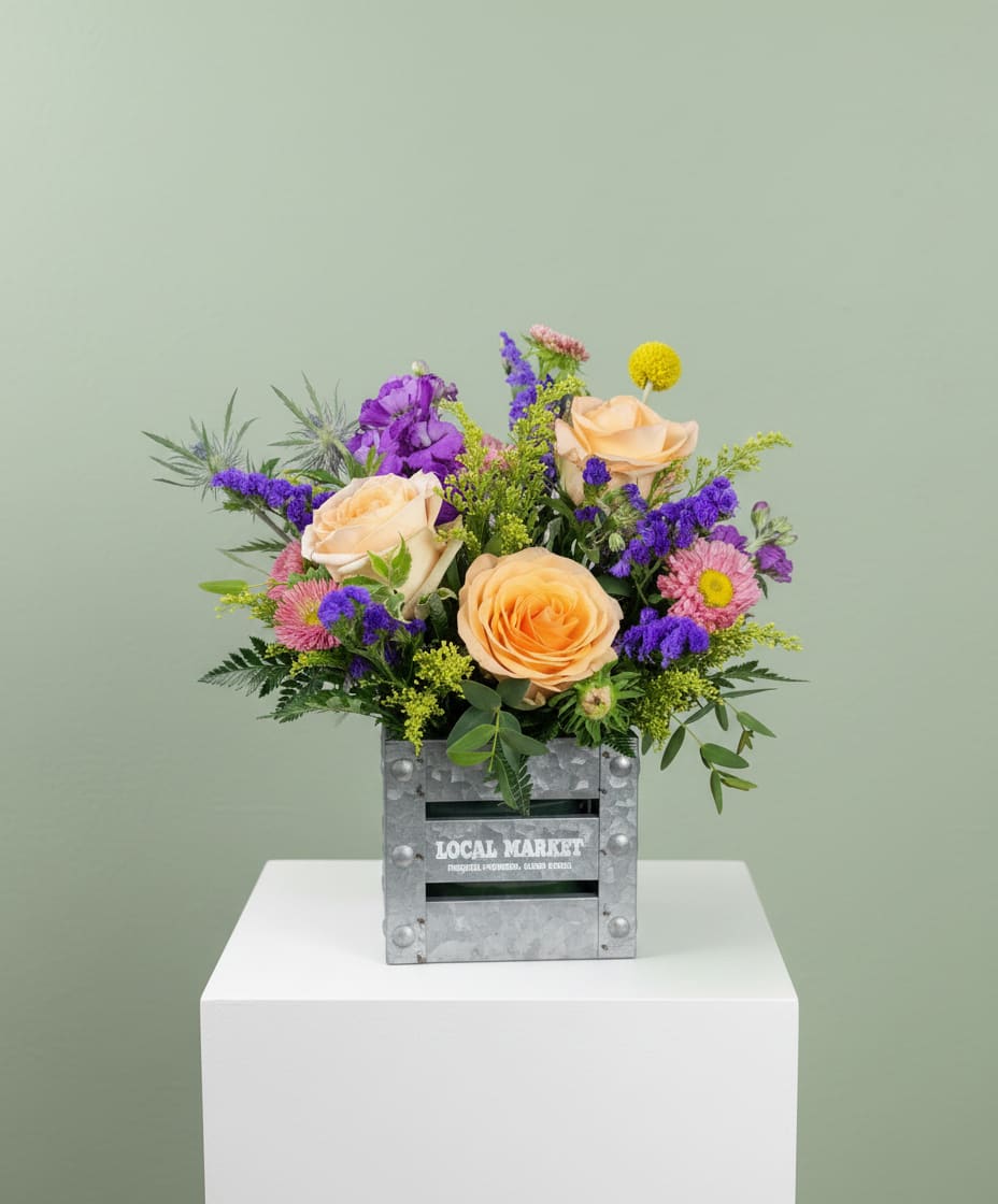 Mixed bouquet of peach roses and purple flowers in a metal crate