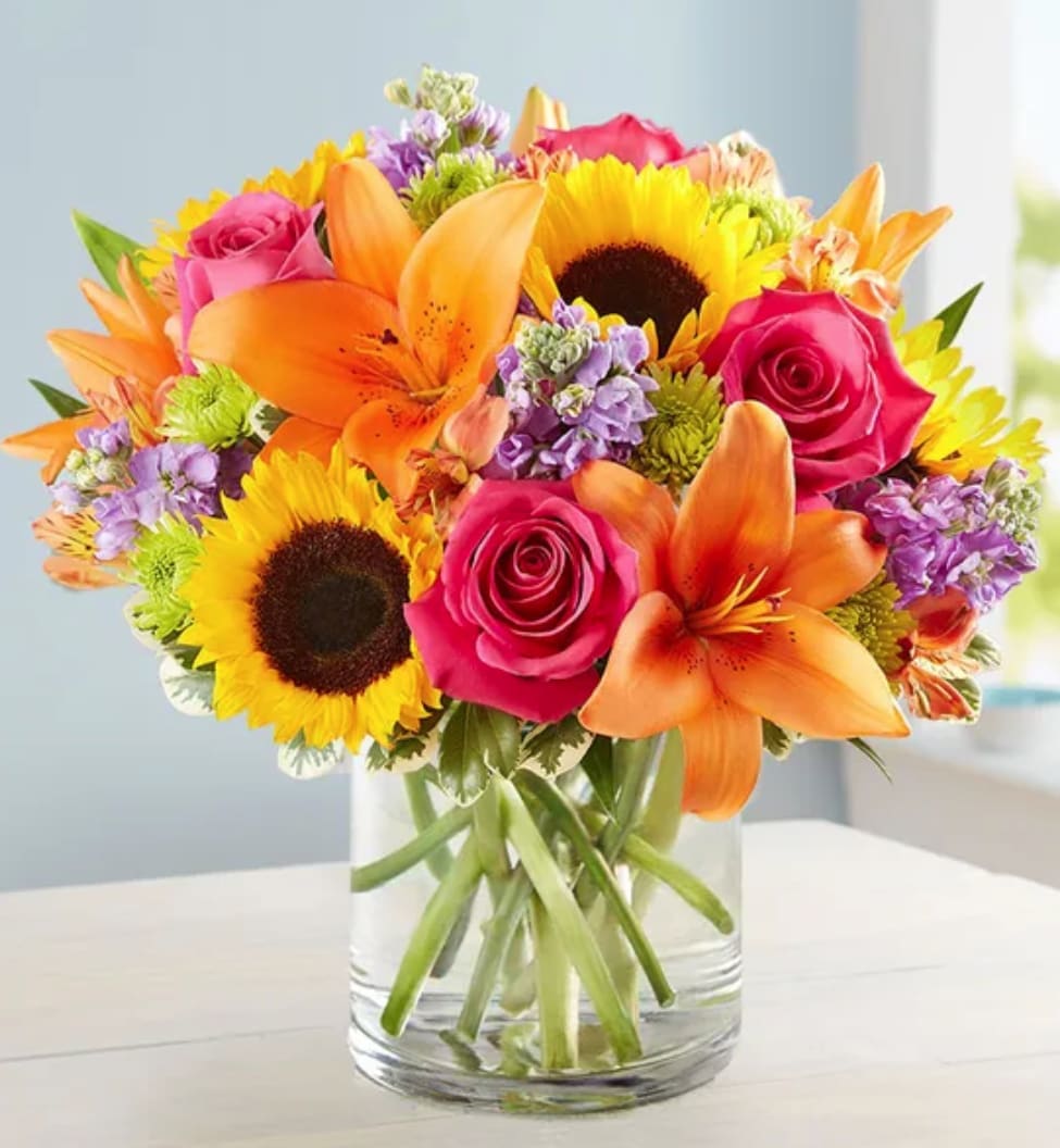 Bright mixed bouquet of roses, lilies, and sunflowers in a glass vase