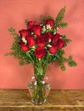 Red roses arranged in a clear glass vase with greenery