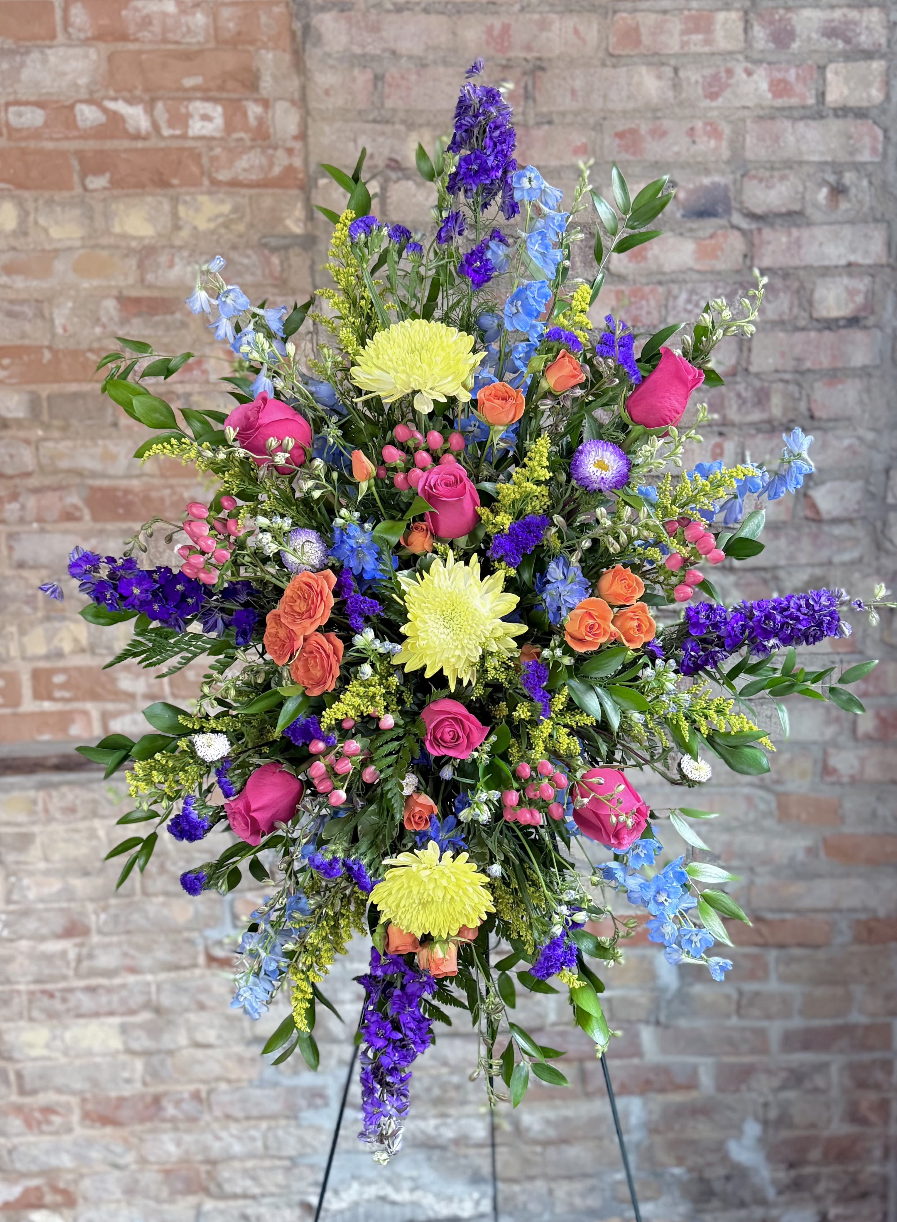Tall mixed flower arrangement with pink roses, yellow mums, and blue-purple blooms