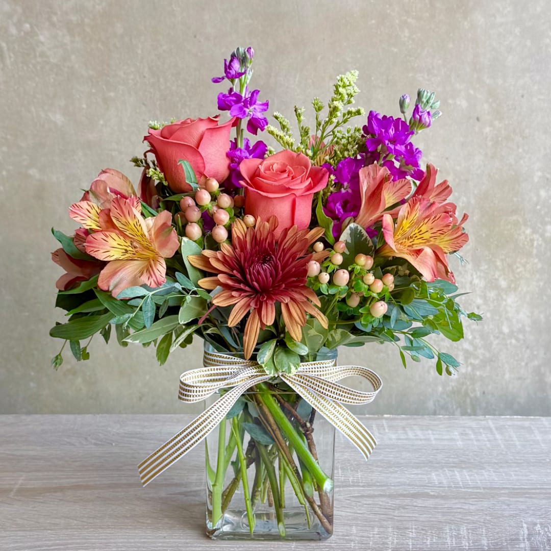 Mixed bouquet of pink roses, purple blooms, and alstroemeria in a glass vase