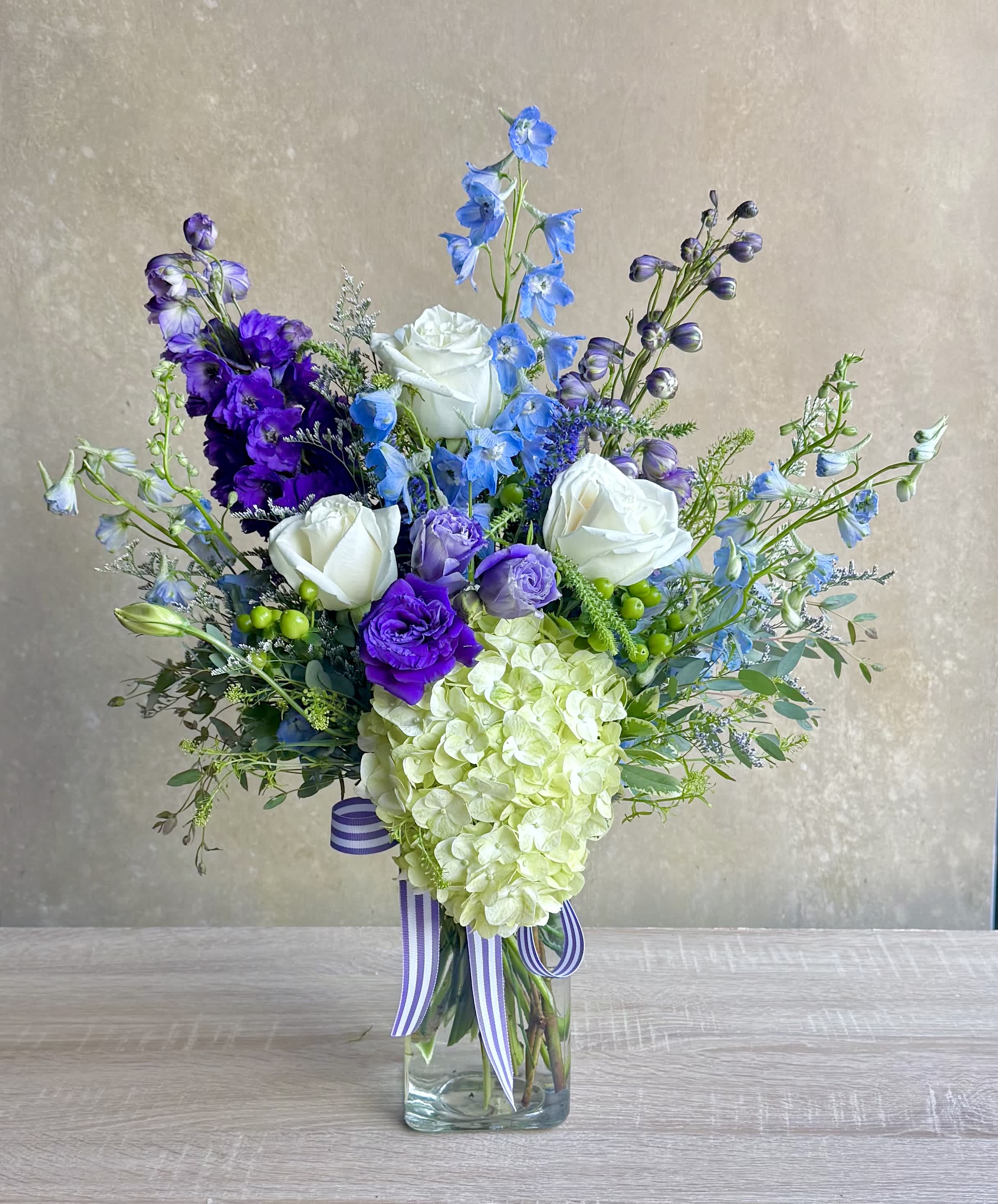 Blue and purple mixed bouquet with white roses in a glass vase