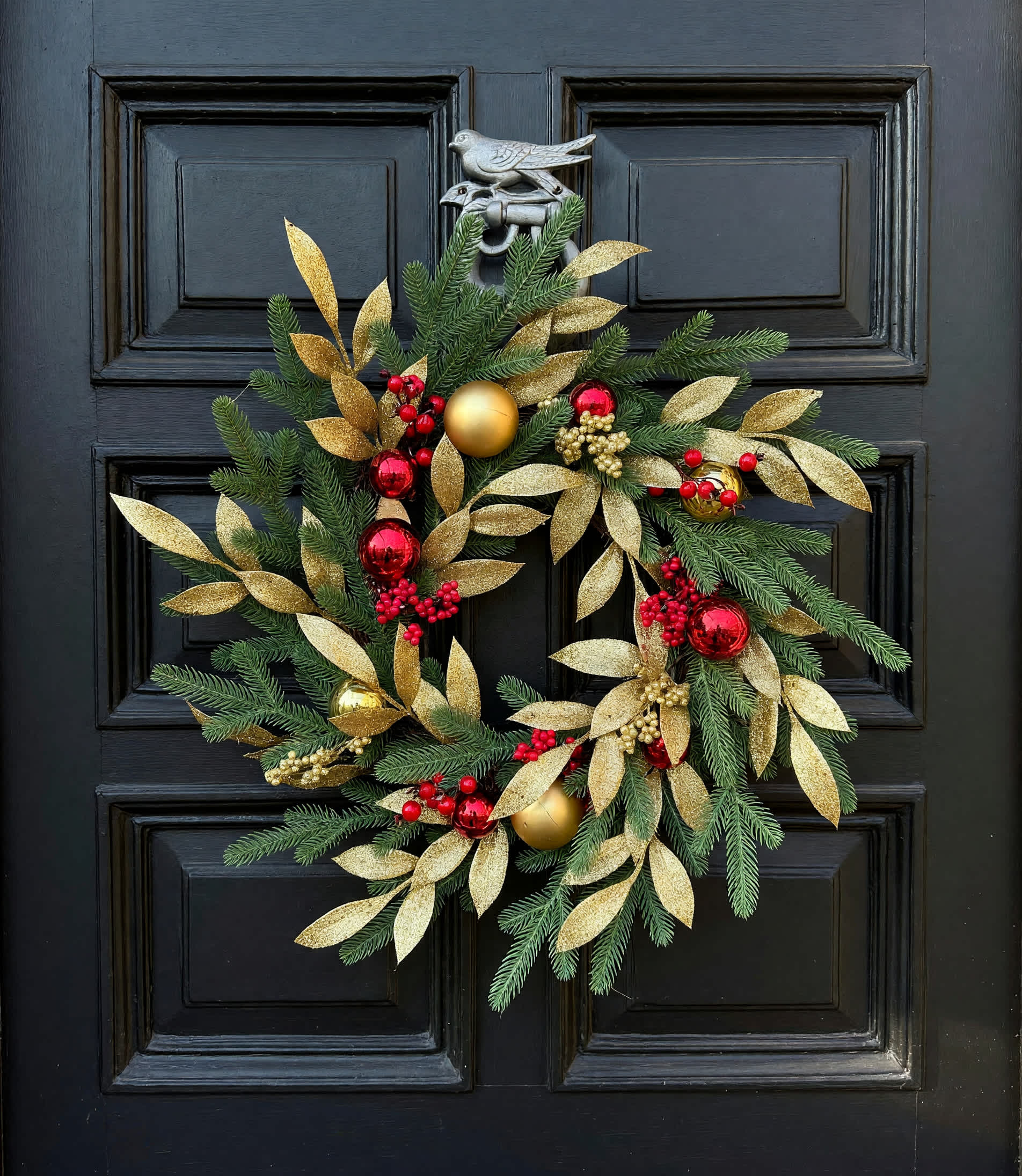 Christmas wreath with gold leaves, red berries, and ornaments on a black door