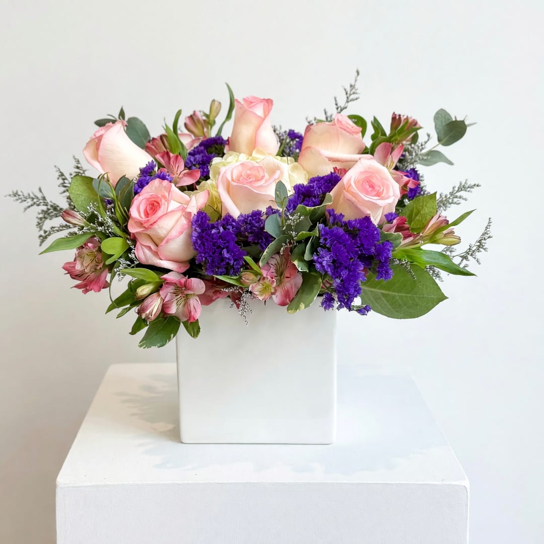 Pink roses and purple flowers arranged in a white square vase