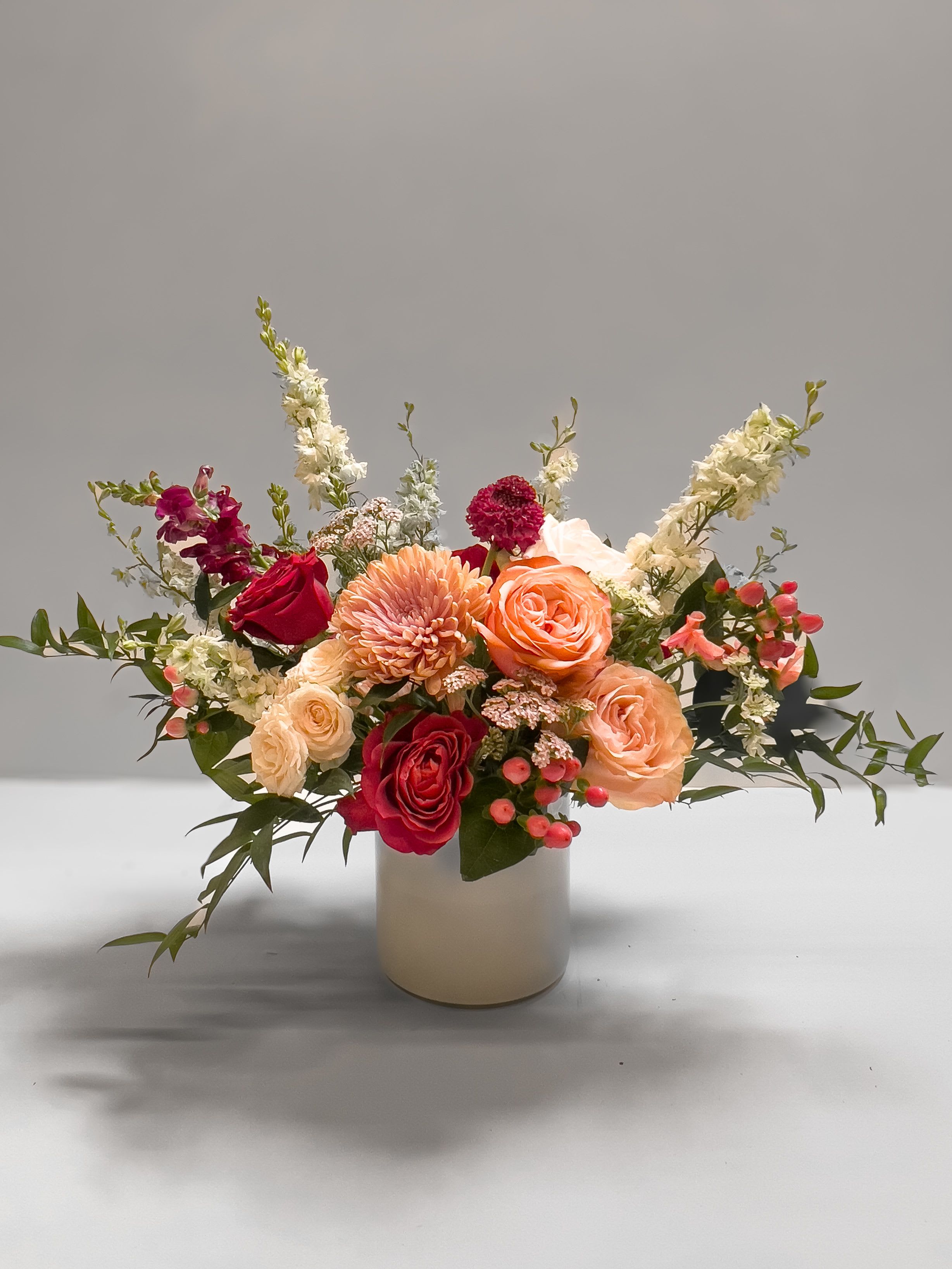 Mixed bouquet of roses, chrysanthemums, and white spikes in a cream vase