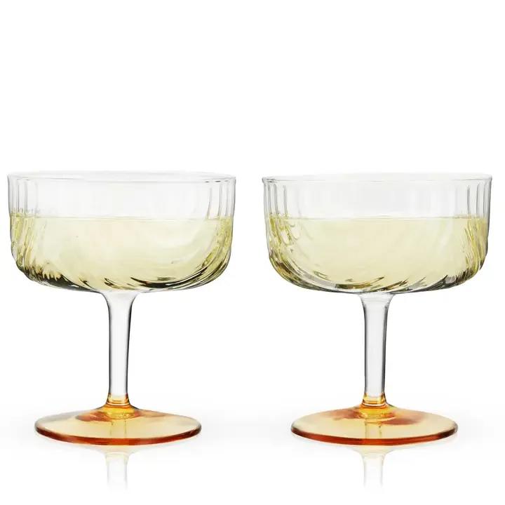 Deco Gatsby Gold-Plated Glass Coupes - Set of 2 - Draping glass and polished gold details give this stemmed glassware set Jazz Age flair. Made from high-quality glass with a gold-plated base, these coupes elevate any cocktail, shaken or stirred. Perfect for Manhattans, Martinis and more!  Quantity: 2 coupes Materials: Glass, gold plating Capacity: 9 oz. Care: Hand wash  Viski, a name that epitomizes sophistication and expert craftsmanship, presents an enchanting selection of high-end glassware, barware, and wine accessories that serve as perfect selections for the autumn season. As you plan a backyard bonfire with friends, host a dinner party on Labor Day with family or choose the perfect fall wedding present, let Viski’s offerings enrich the celebration of these crisp, cool days. Our products not only raise the bar of mixology but also add a touch of luxury to any home bar, making every fall occasion memorable.