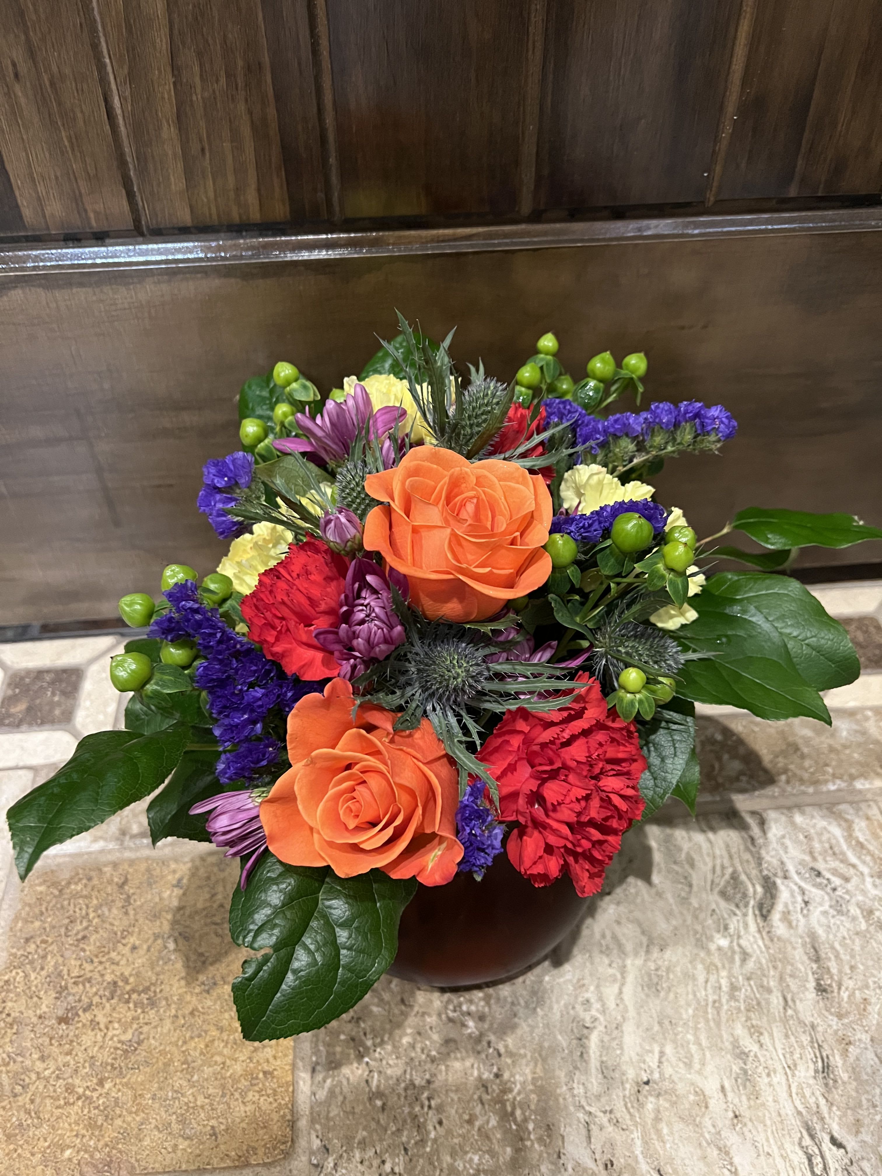 Colorful bouquet with orange roses and purple, red, and yellow flowers in a vase