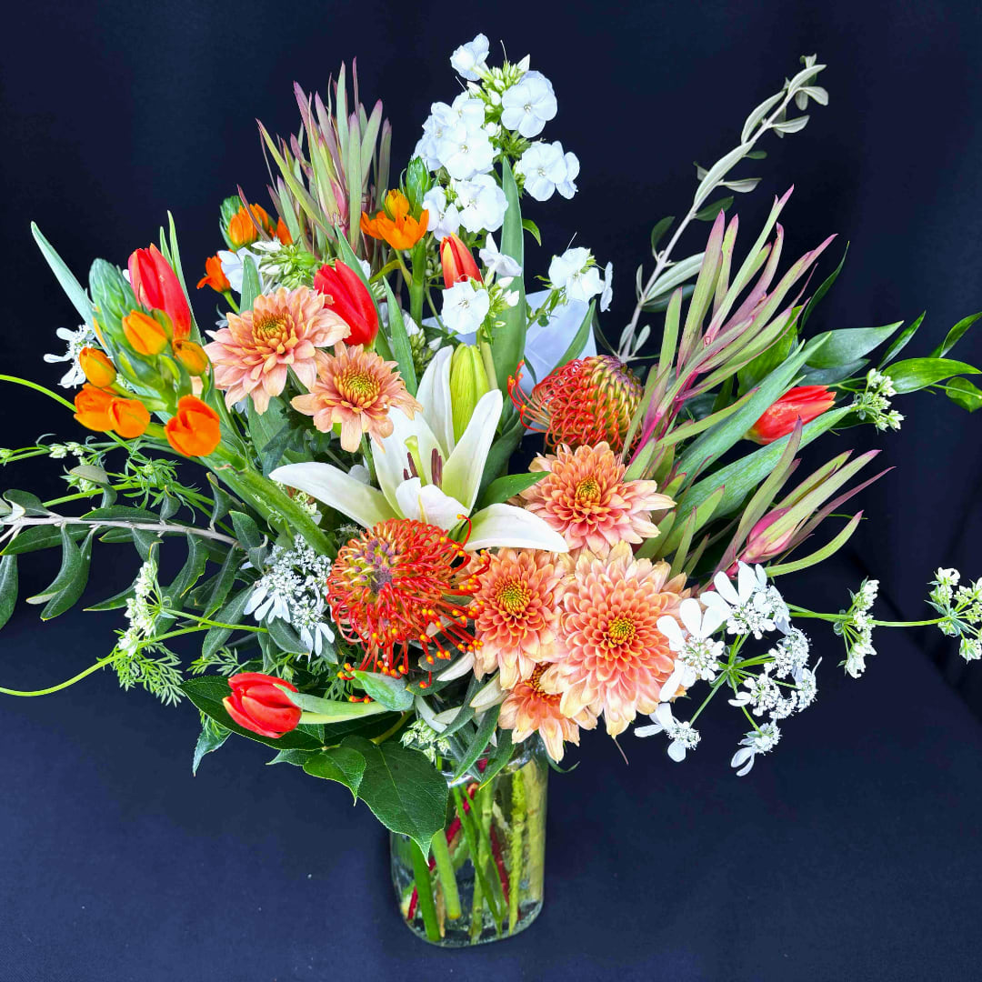 Mixed bouquet in a clear glass vase with white, orange, and peach blooms