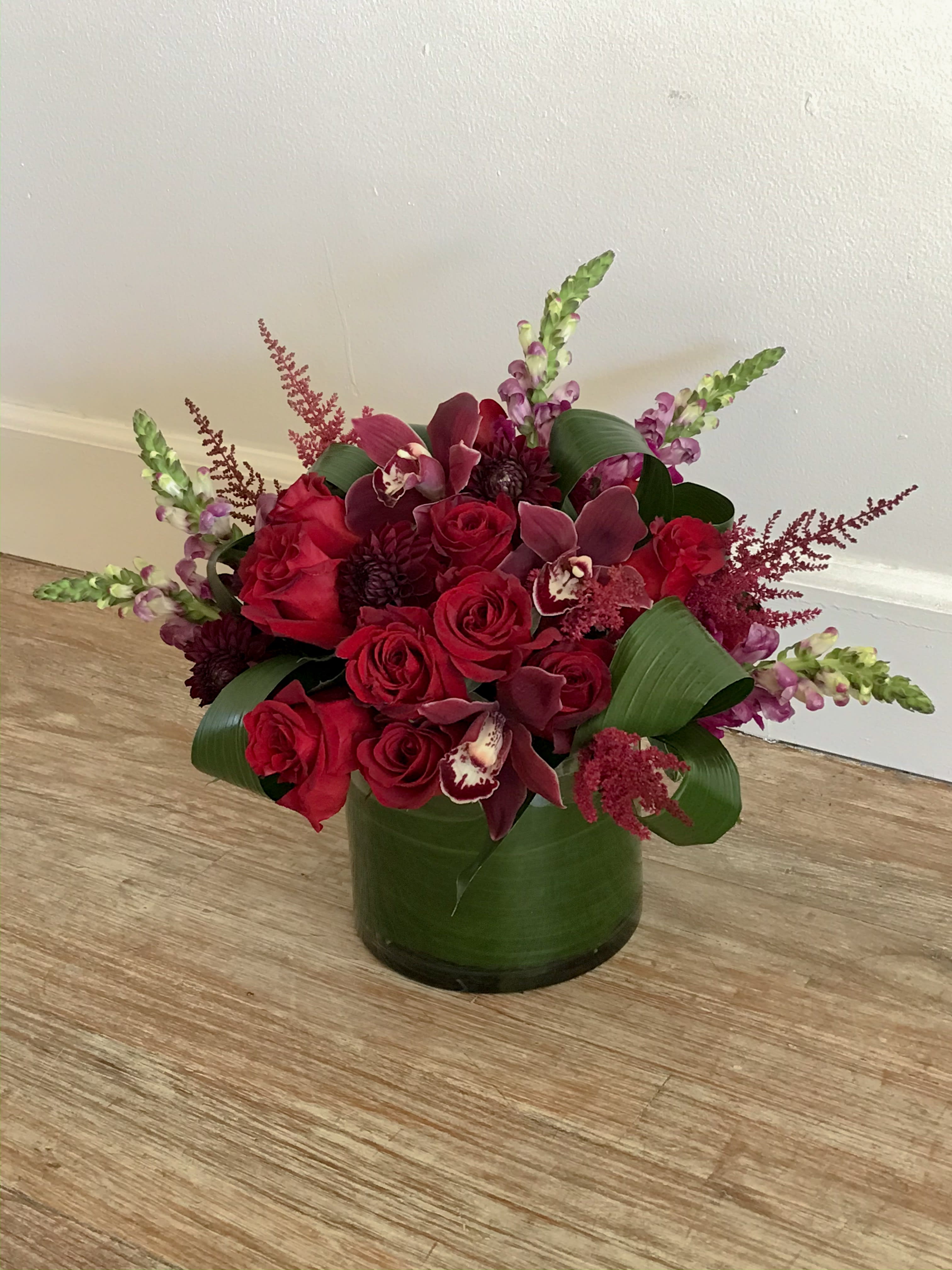 All You Need Is Love - This arrangement is full of deep rich reds with lots of texture.  Roses and cymbidium orchids mixed with seasonal flowers. Colors as well as flowers may be substituted due to availability.