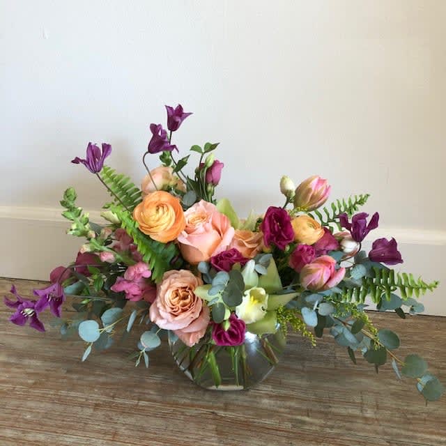 September Song - A beautiful jewel-toned still-life arrangement in peach, purple and pink tones paired with seasonal greens.   Available in other colors ***Flowers may be substituted due to availability.  