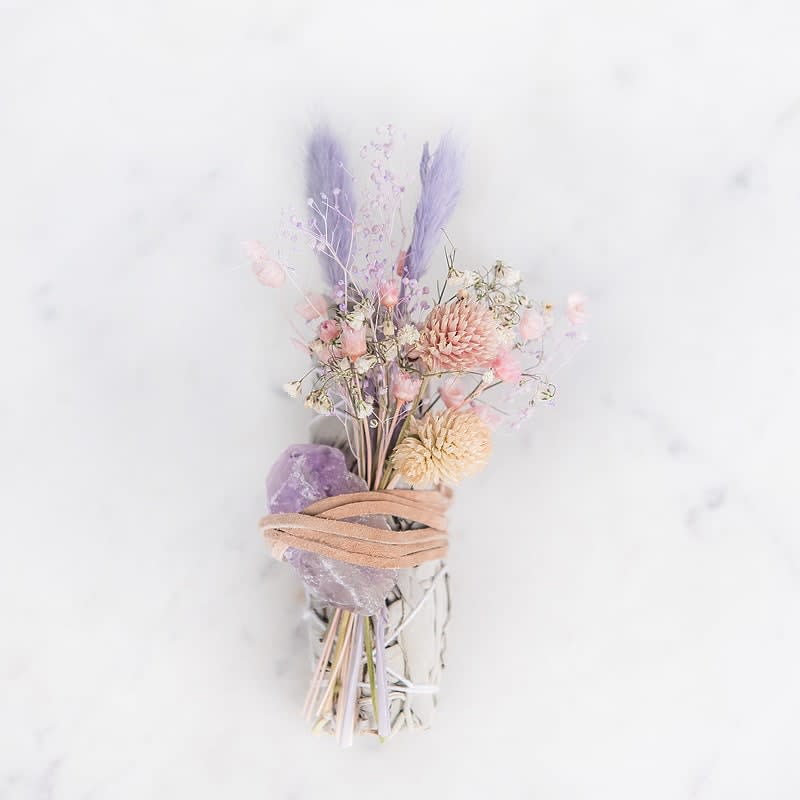 Smudge bundle with amethyst crystal and pastel dried flowers tied with suede cord on white background
