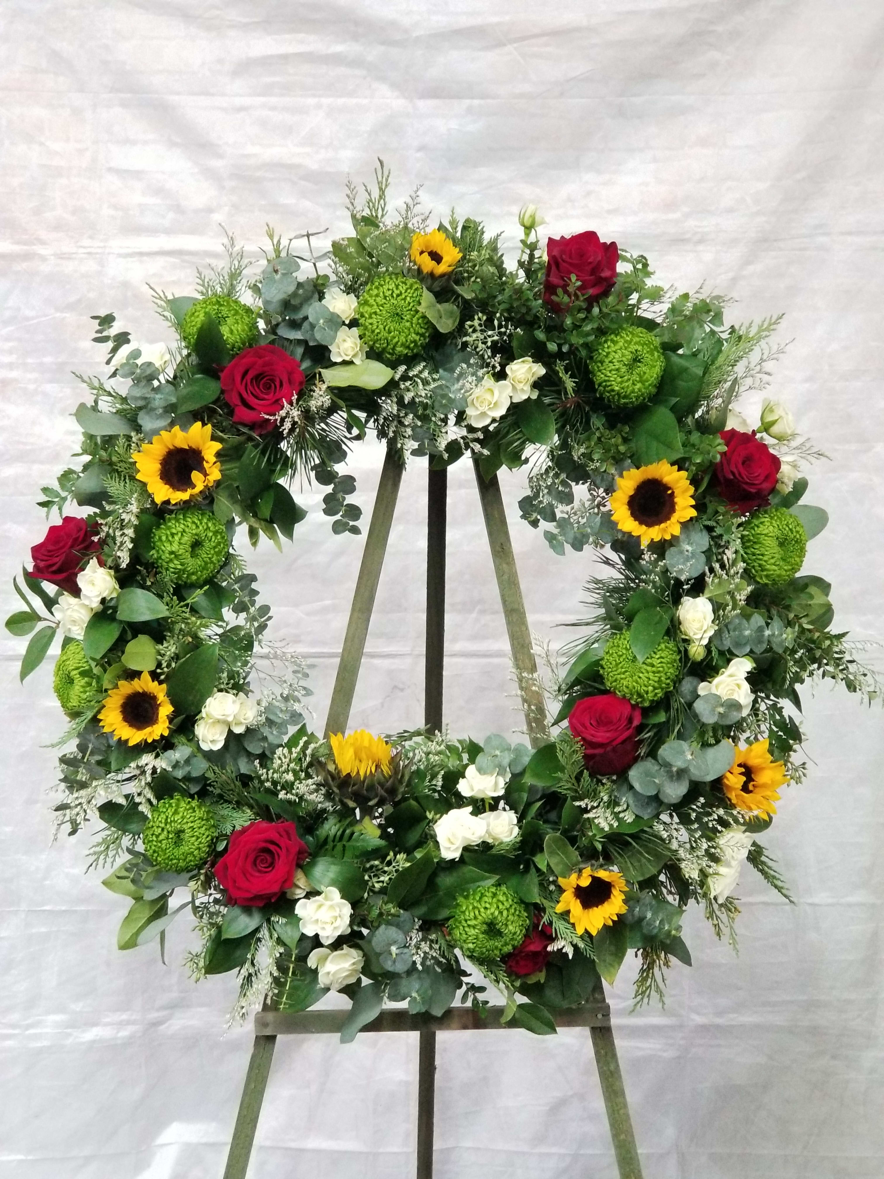 Large floral wreath with red roses, sunflowers, and green mums on an easel