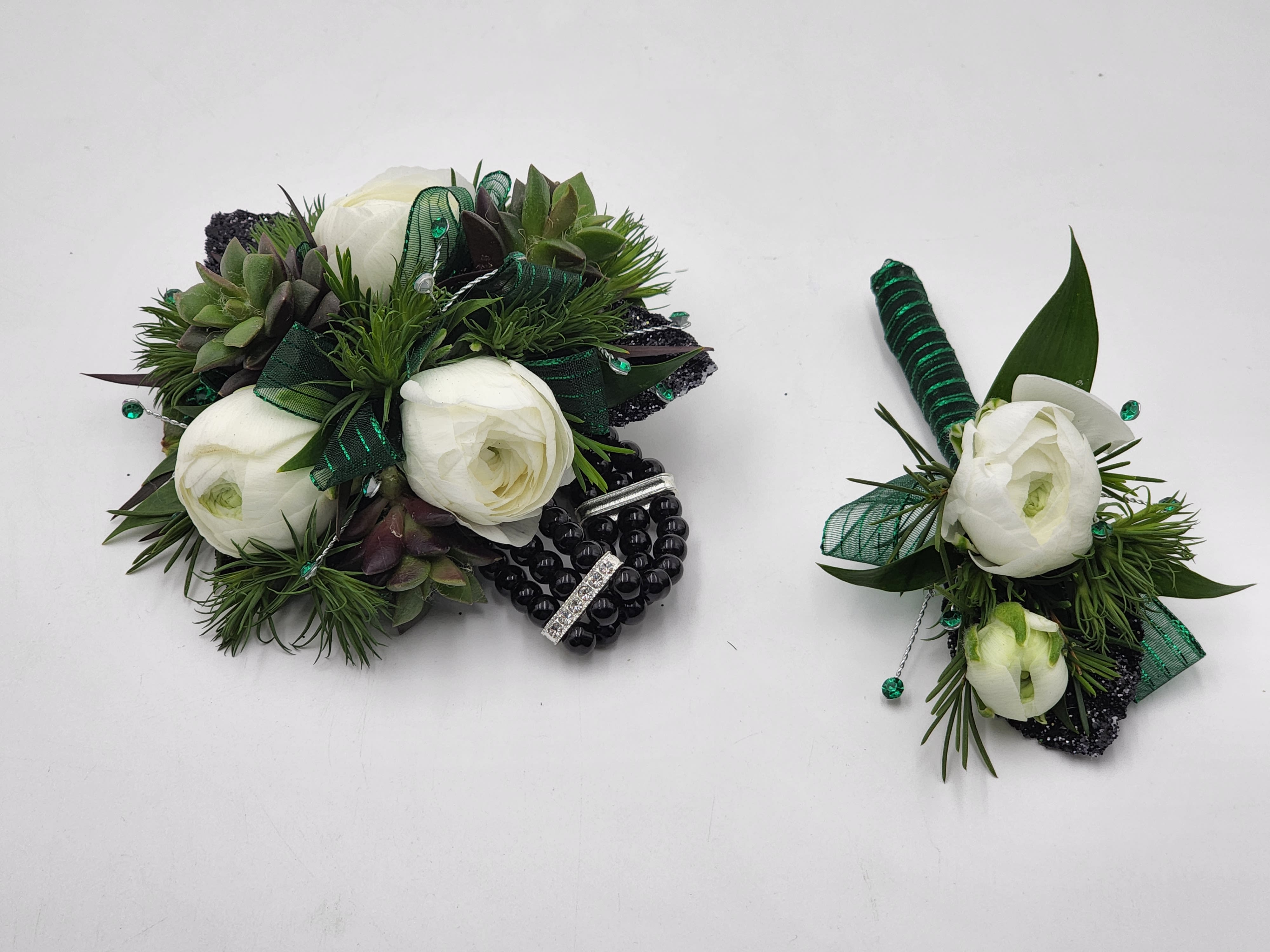 Fern Valley Boutonniere And Wristlet Set - A boutonniere and wrist corsage set of white ranunculus, succulents, green ribbon and a black keepsake bracelet.  Depending on availability of ribbon, may change slightly.