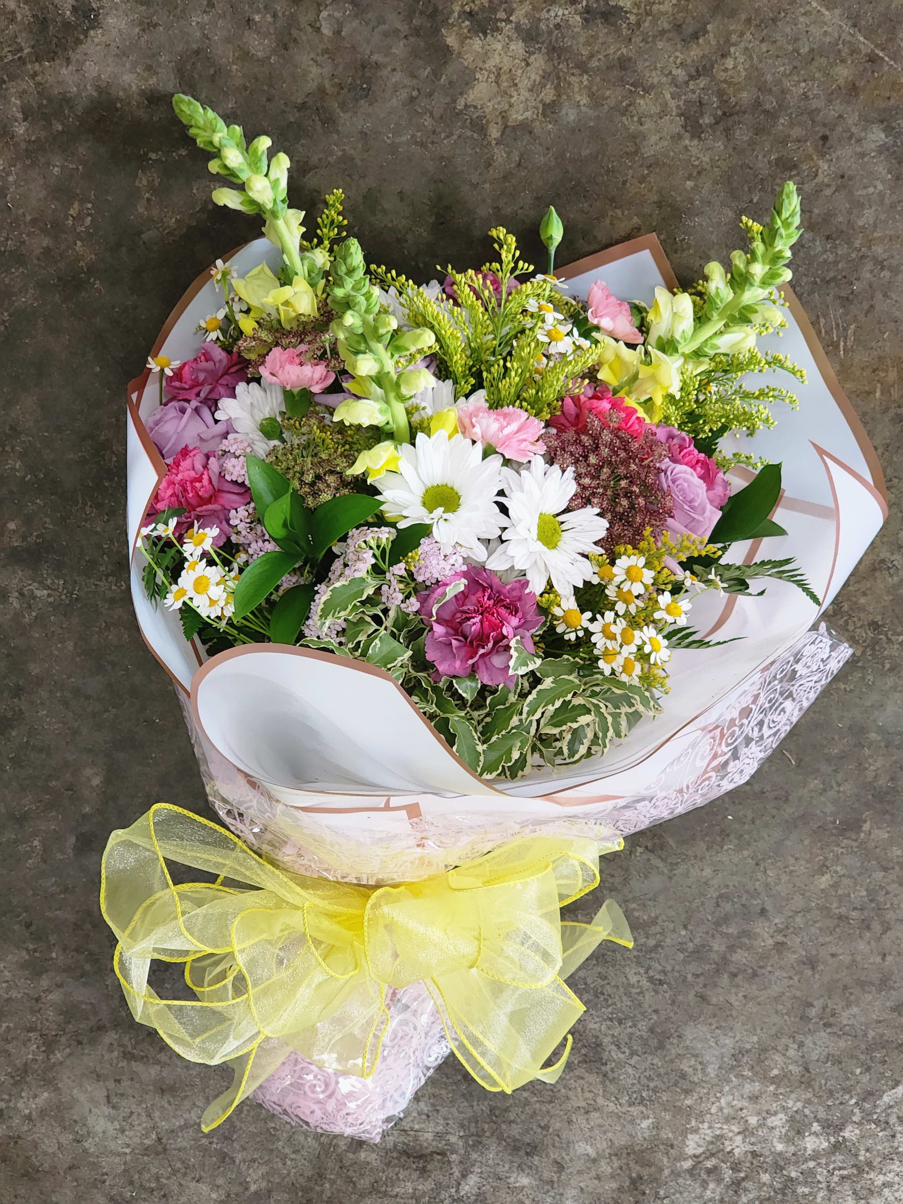 Mixed bouquet of pink, white, and yellow flowers wrapped with a yellow ribbon