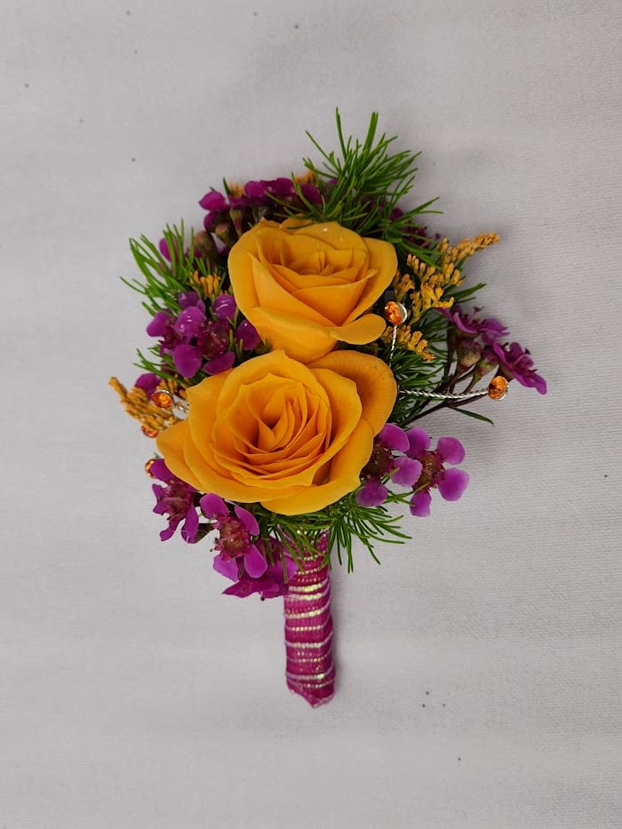 Fantasia Boutonniere - Select this colorful boutonniere featuring spray roses, waxflower, and misty with accents of orange rhinestones and pink ribbon. The boutonniere will come with two black pins to pin on their lapel or shirt.
