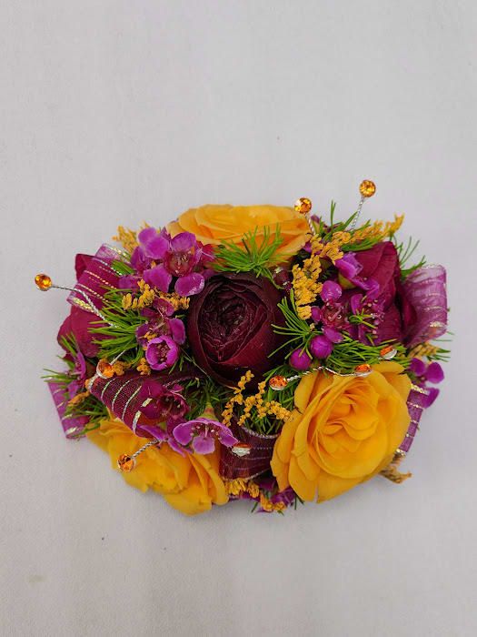 Fantasia Wristlet - Select this colorful wristlet corsage set featuring ranunculus, spray roses, waxflower, and misty with accents of orange rhinestones and pink ribbon. The wristlet corsage will come on a standard grey wristband that is elastic. 