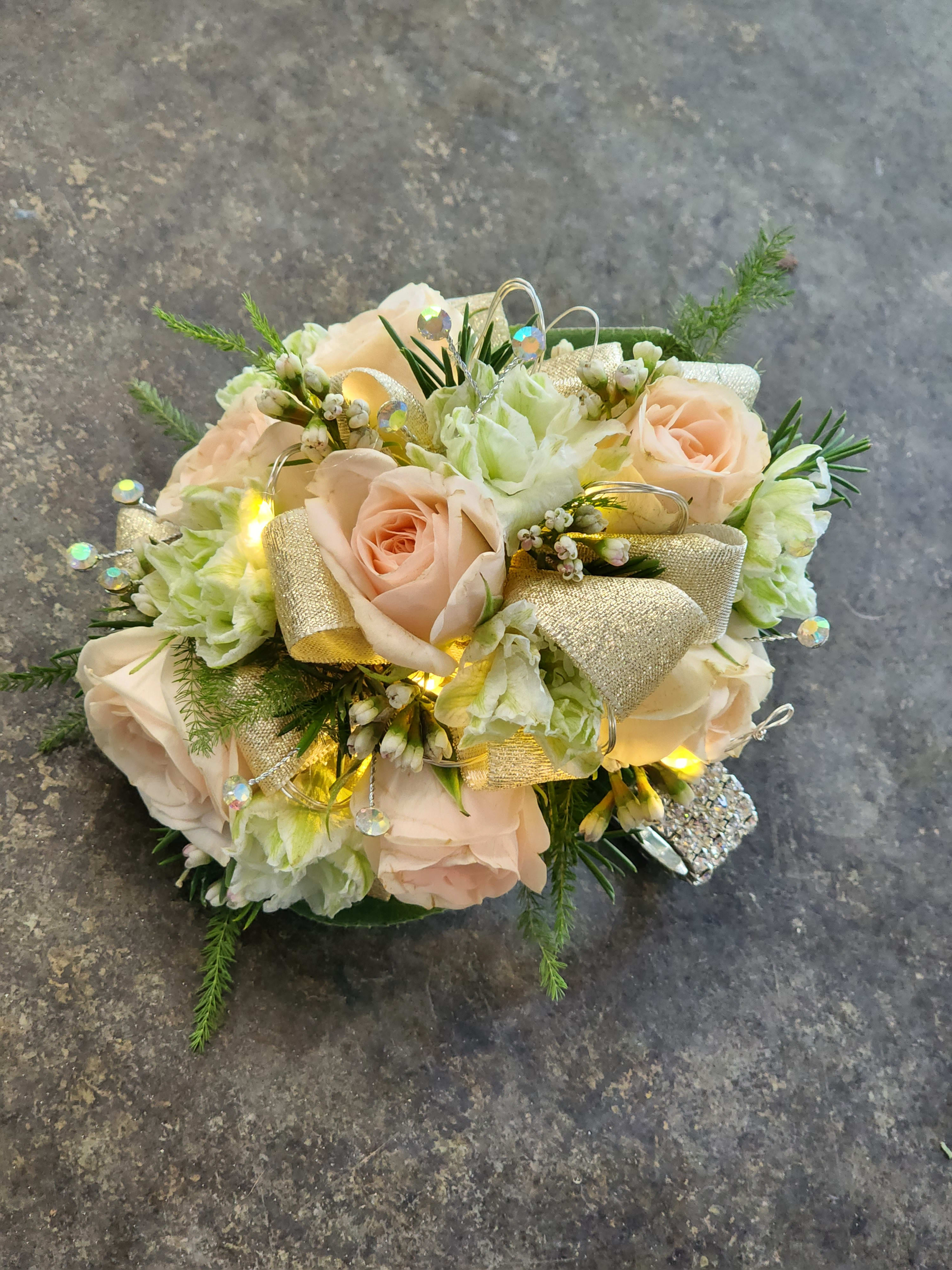 Festival of Lights Wristlet - A wrist corsage with light pink spray roses, white larkspur blooms, rhinestones and a sparkly keepsake bracelet. The corsage also features lights that turn on and brighten up the night.